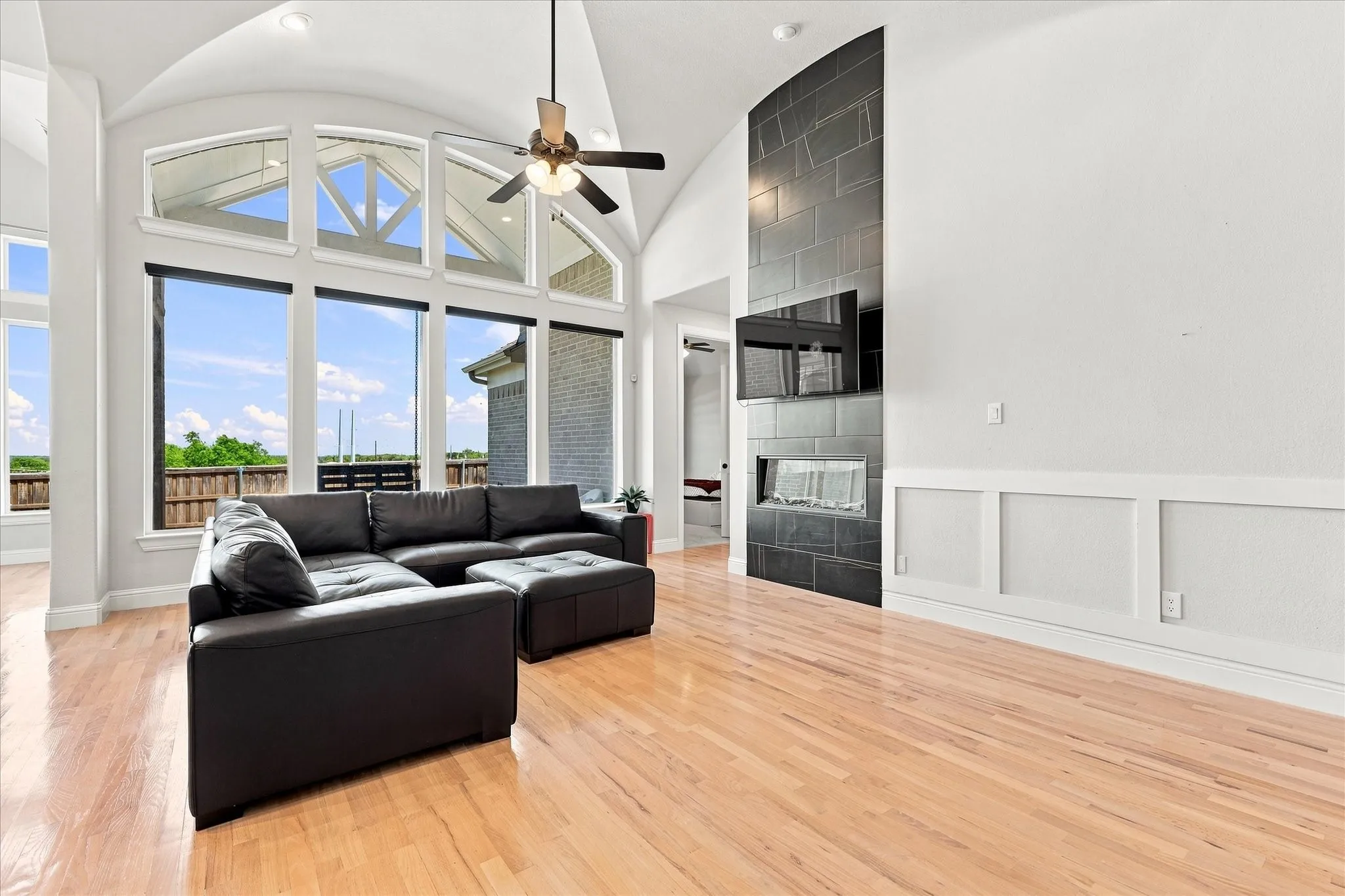 Vaulted ceiling with a ceiling fan, expansive windows, wood-finish flooring, and a modern fireplace with a tiled surround
