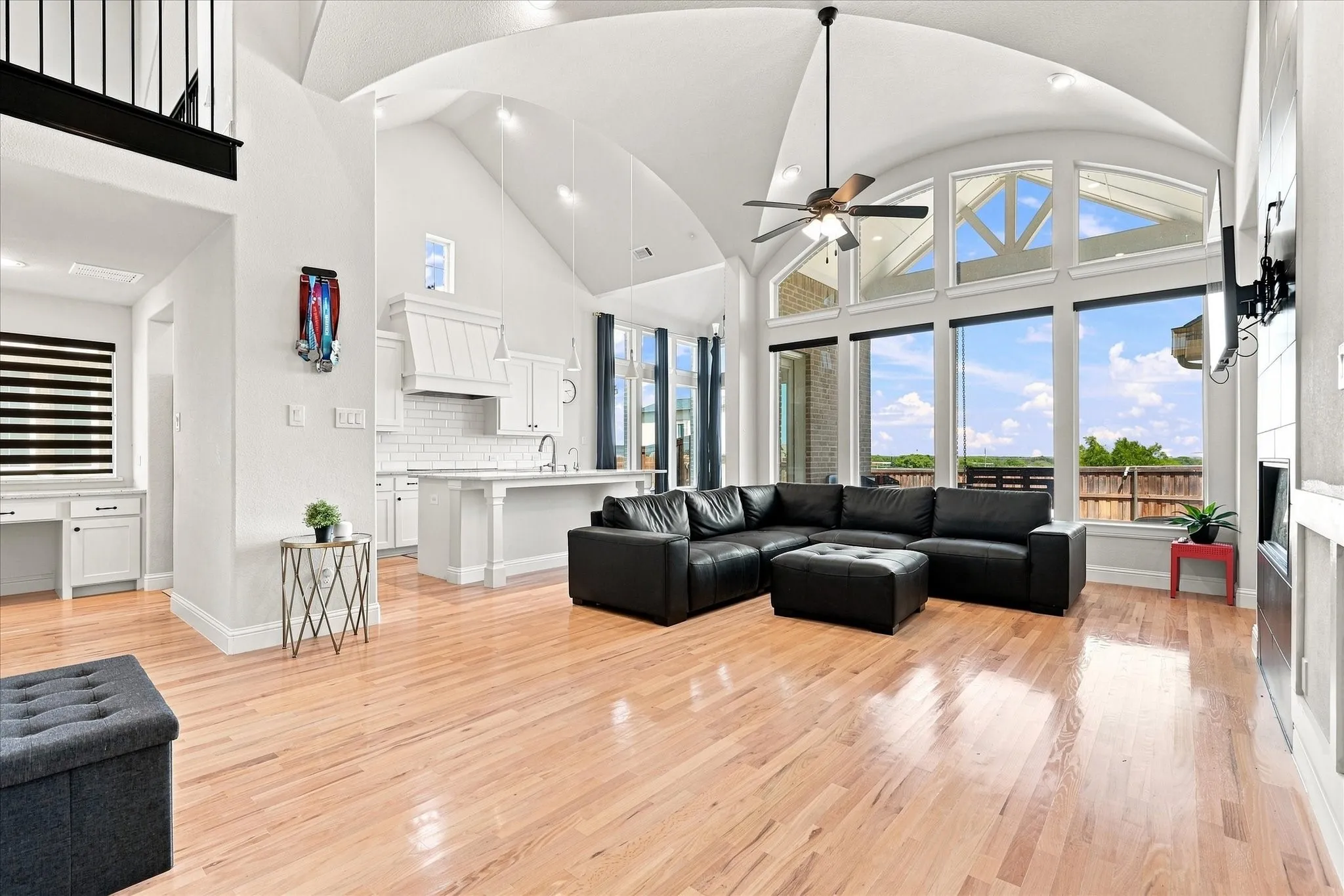 Arched ceiling with exposed beams, expansive windows, light wood-finish flooring, built-in kitchen island, and a built-in desk area