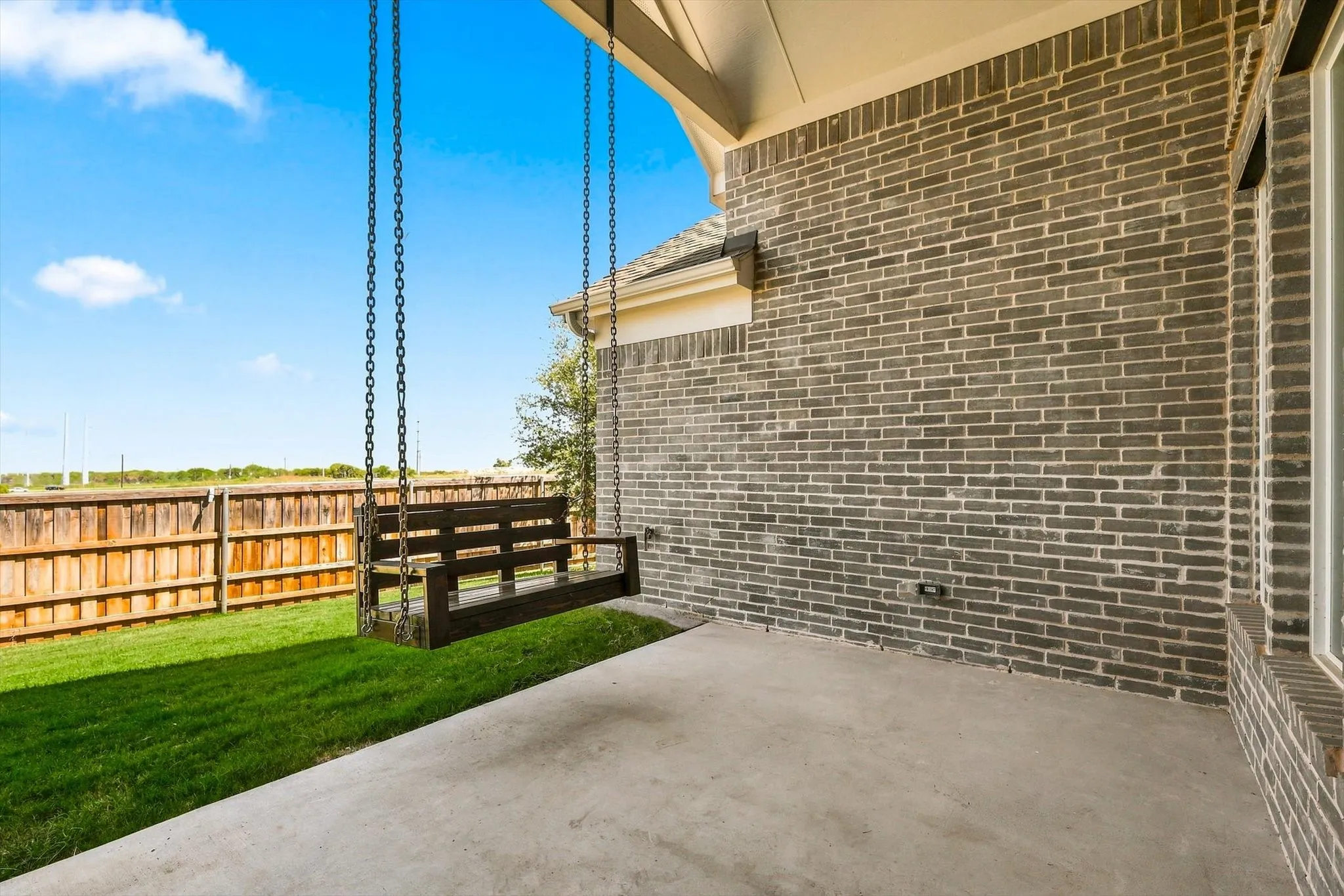 Covered patio with a concrete slab, dark brick exterior, and a wood privacy fence