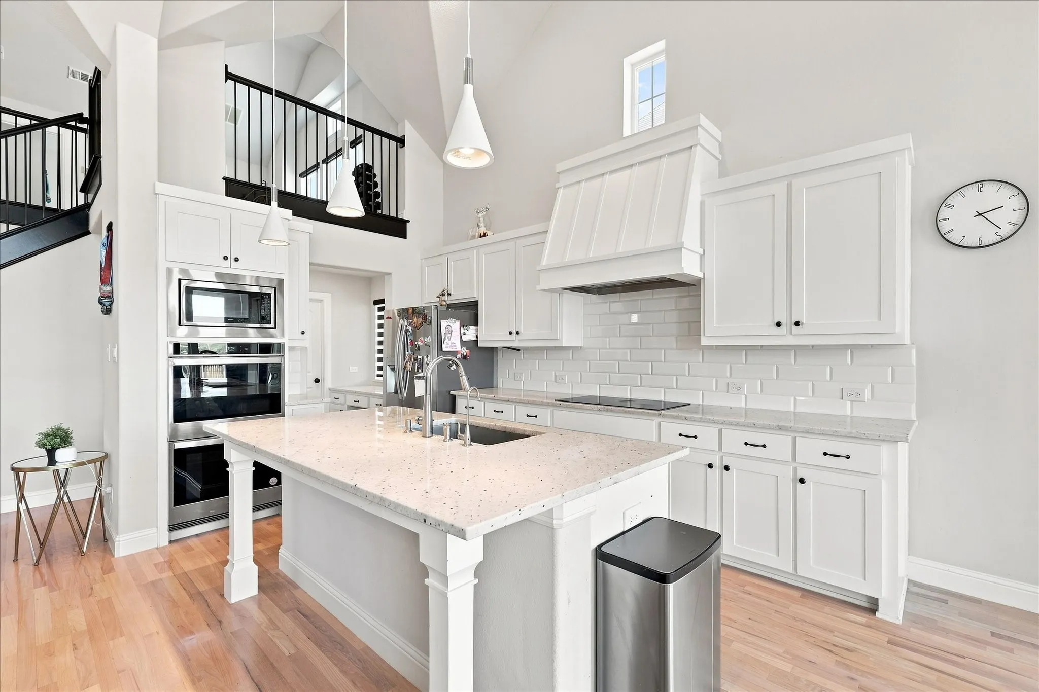 Kitchen featuring white cabinetry, built-in stainless steel appliances, a center island with a sink, white subway tile backsplash, and light wood-finish flooring