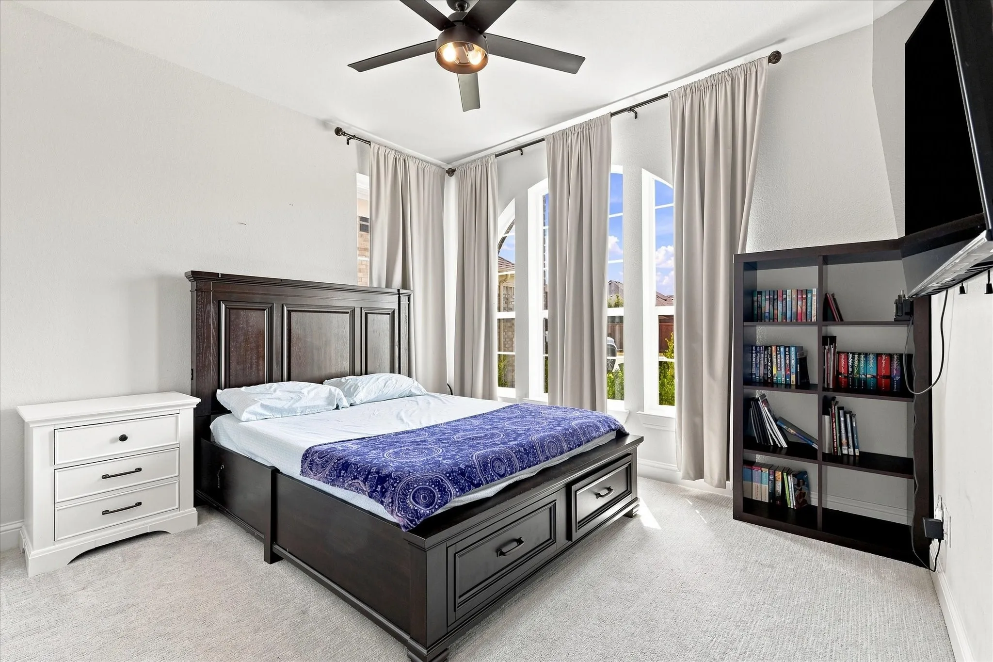 Arched windows with drapery, ceiling fan with integrated lighting, and carpeted flooring