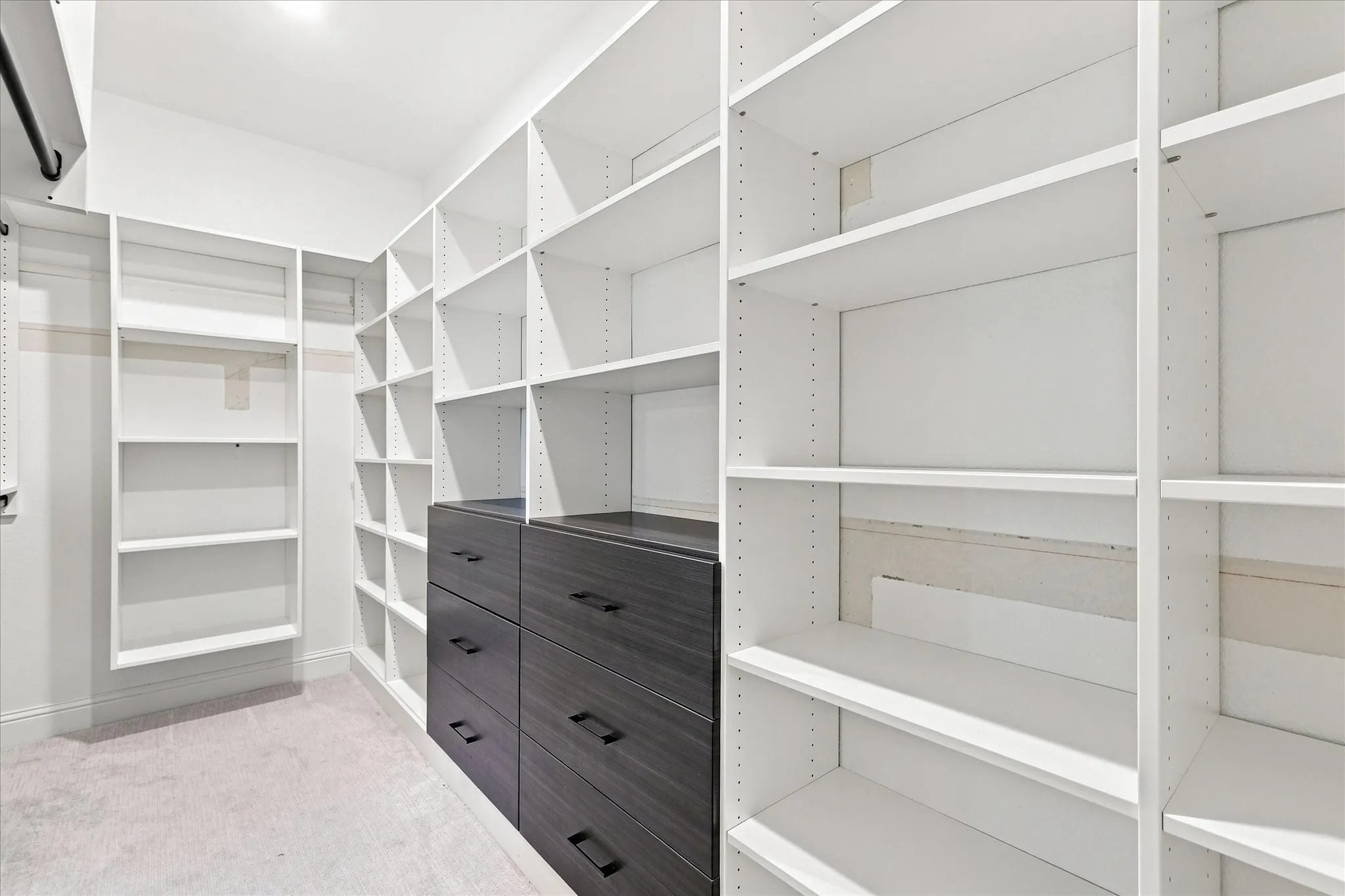 Built-in shelving, integrated wood-finish drawers with dark hardware, hanging rod, and recessed lighting