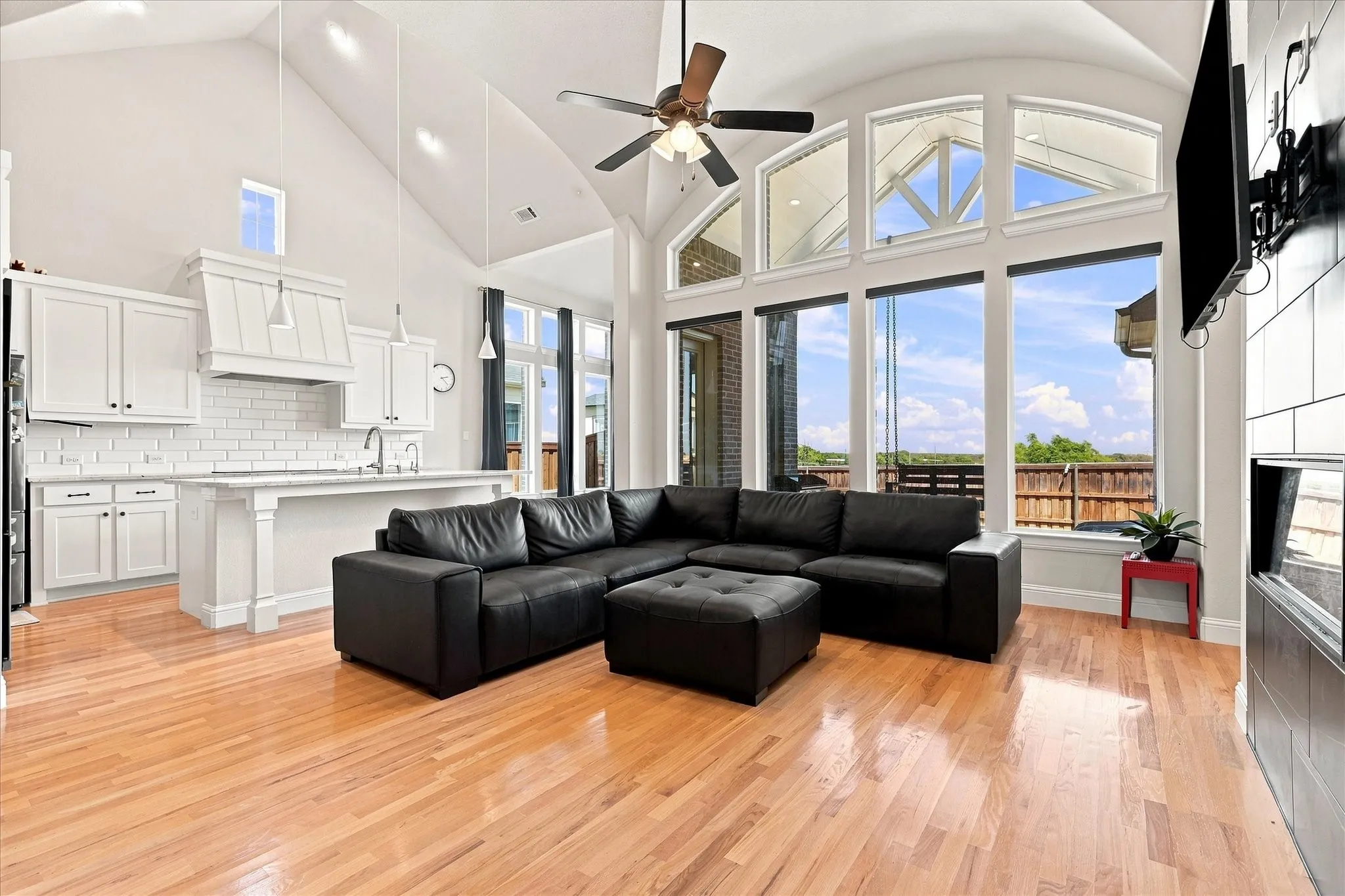 Vaulted ceilings, wood-finish flooring, white kitchen cabinetry, subway tile backsplash, and expansive windows