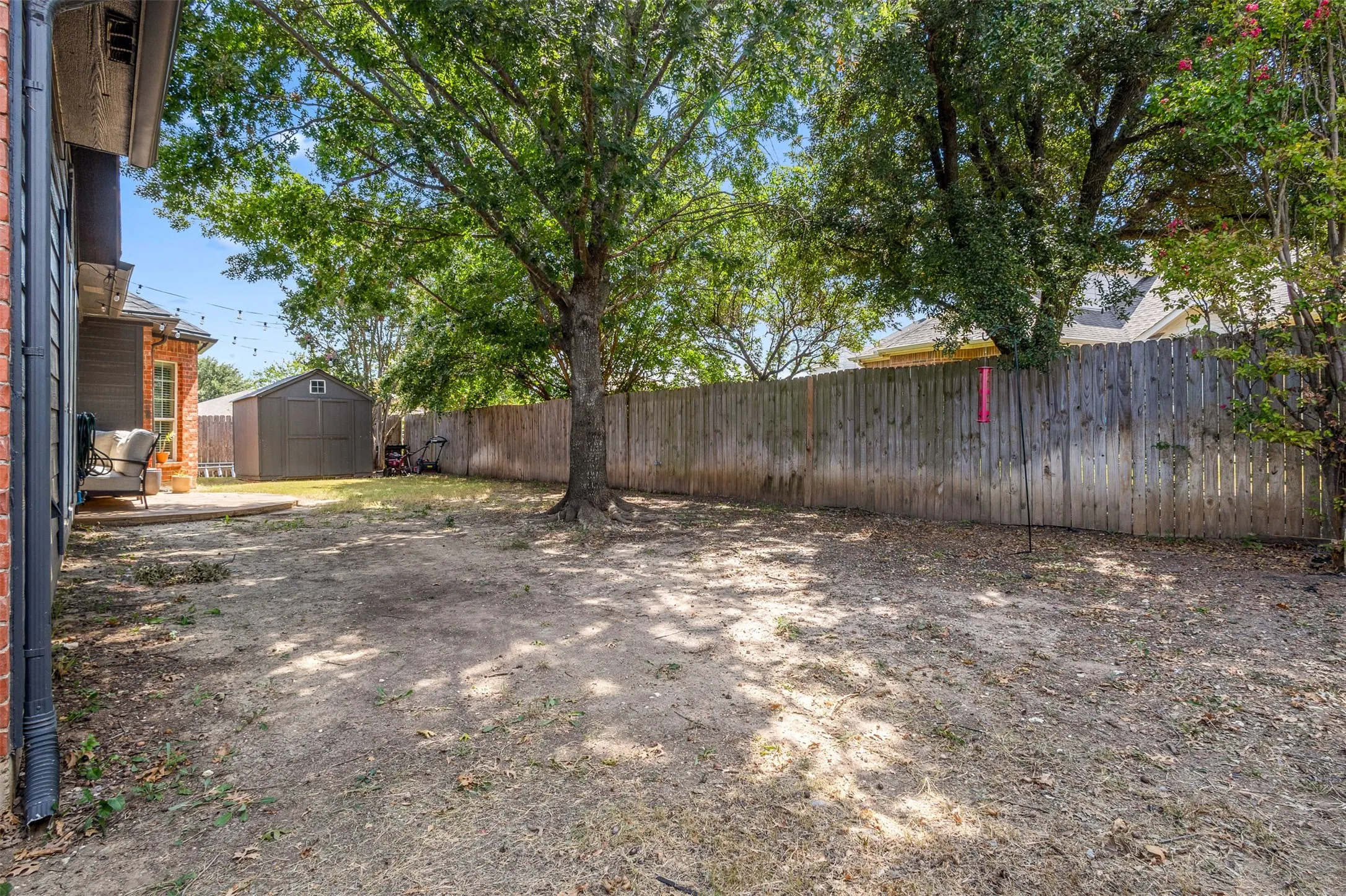 Expansive backyard featuring mature trees, a privacy fence, a concrete patio, and a storage shed