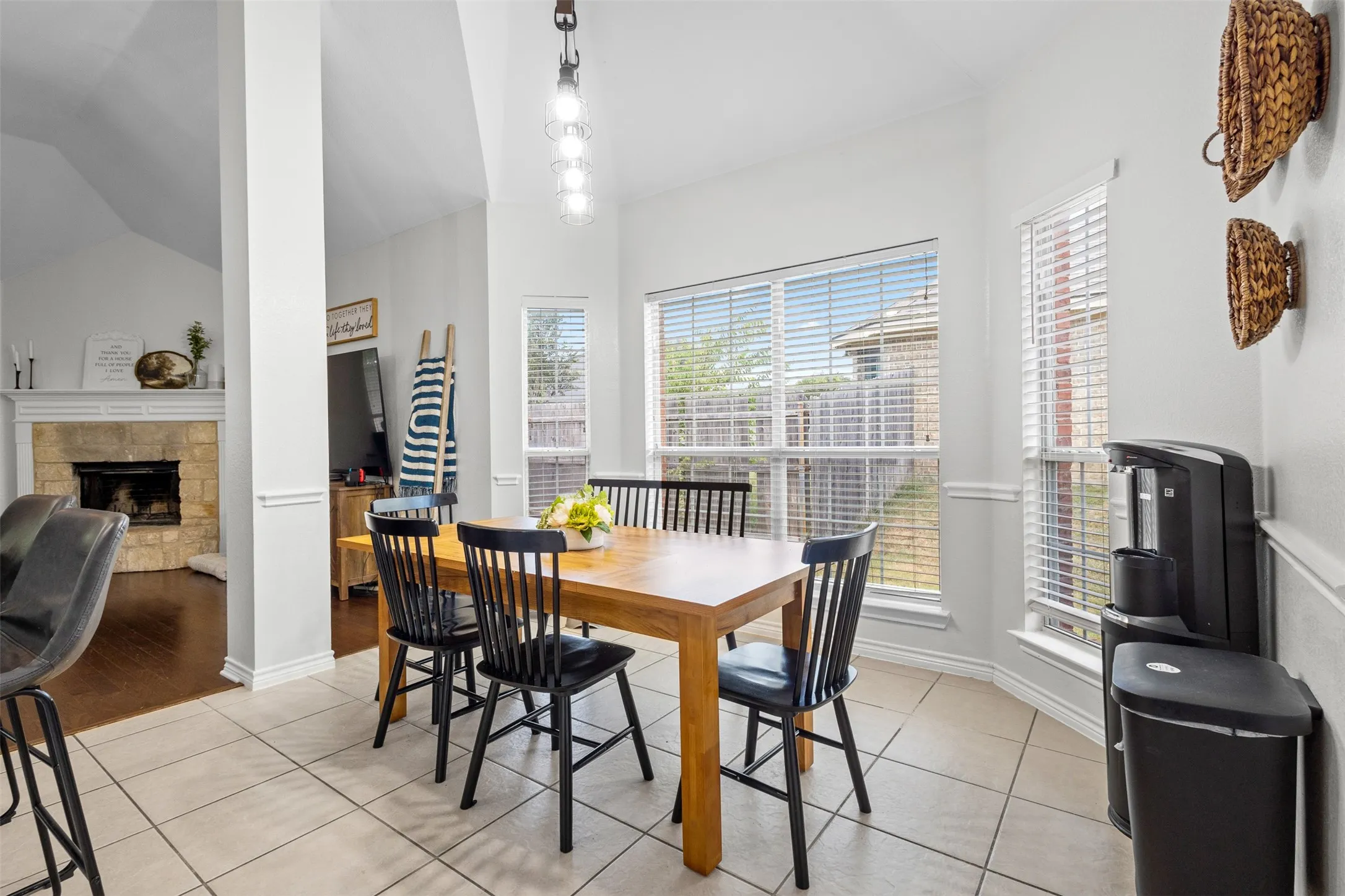 Tile flooring, vaulted ceiling, bay windows with blinds, stone-clad fireplace with mantel, and wood-finish flooring