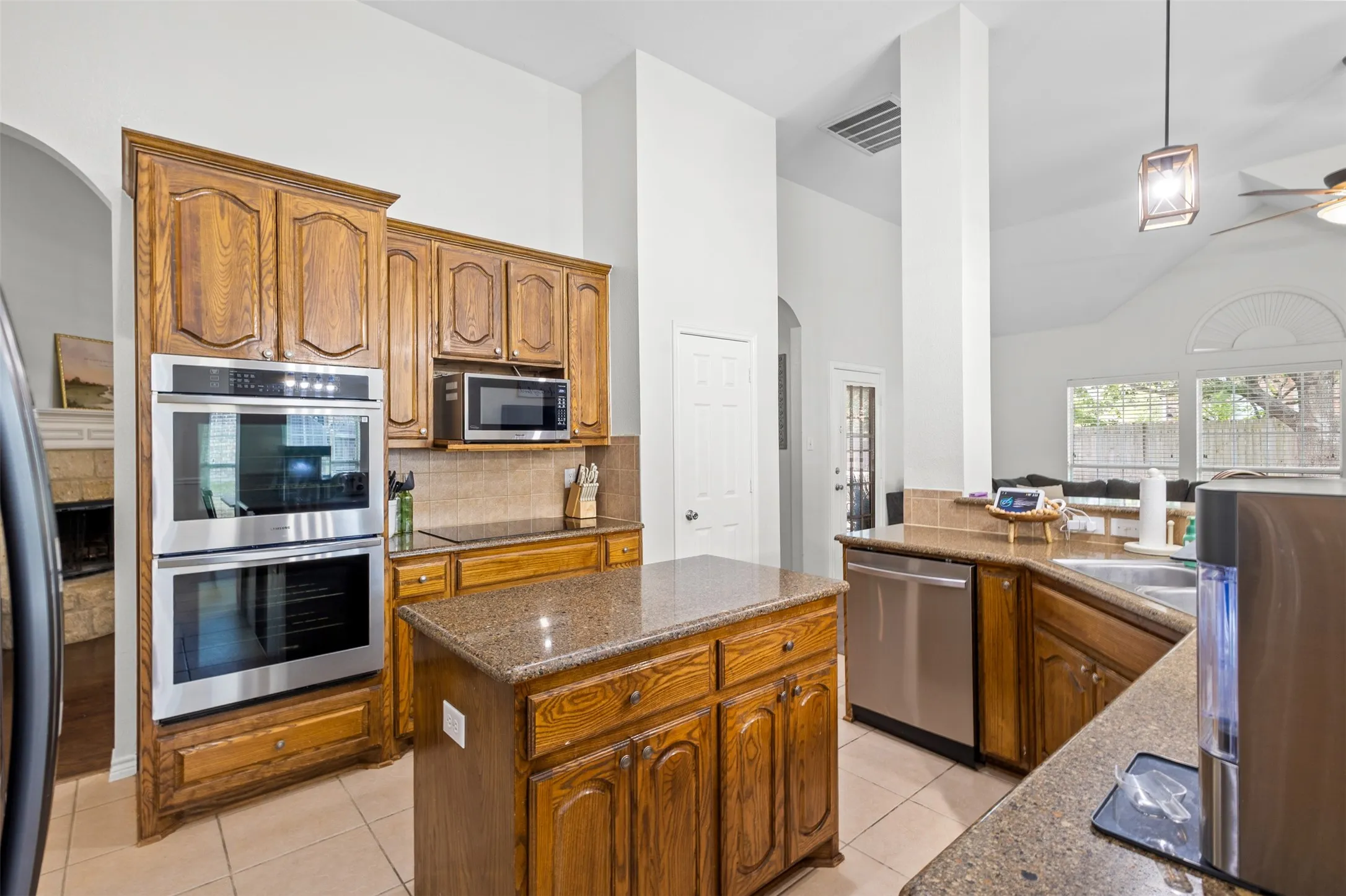 Kitchen featuring wood cabinetry, stainless steel double wall ovens, a central island, and a tile backsplash