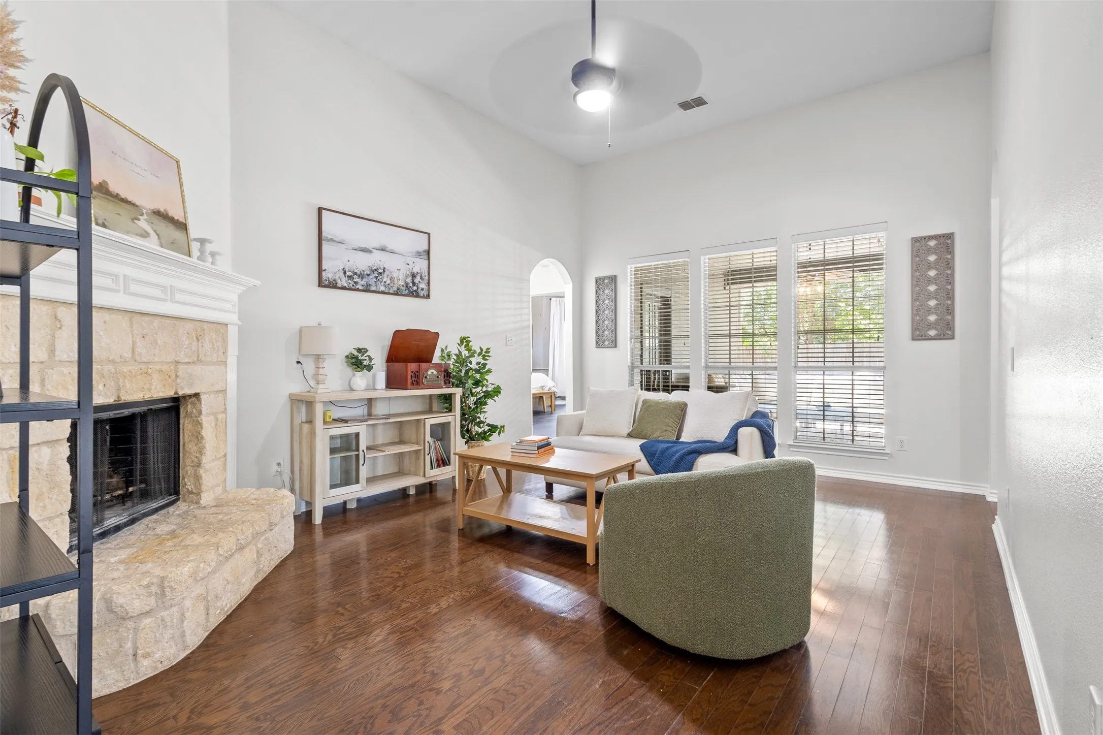 Vaulted ceilings, a stone fireplace, wood-finish flooring, and expansive windows