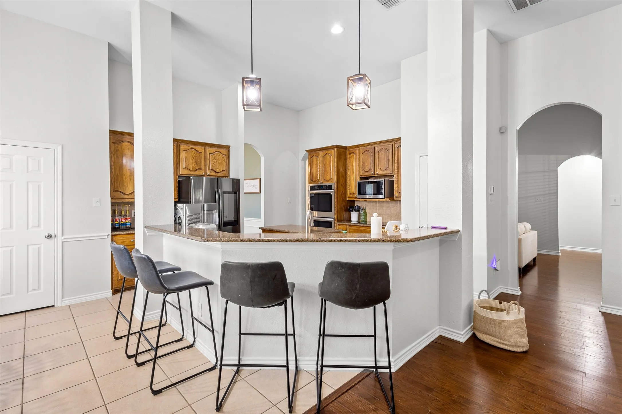 Kitchen featuring wood cabinetry, built-in stainless steel appliances, a breakfast bar with a granite-style countertop, and pendant lighting