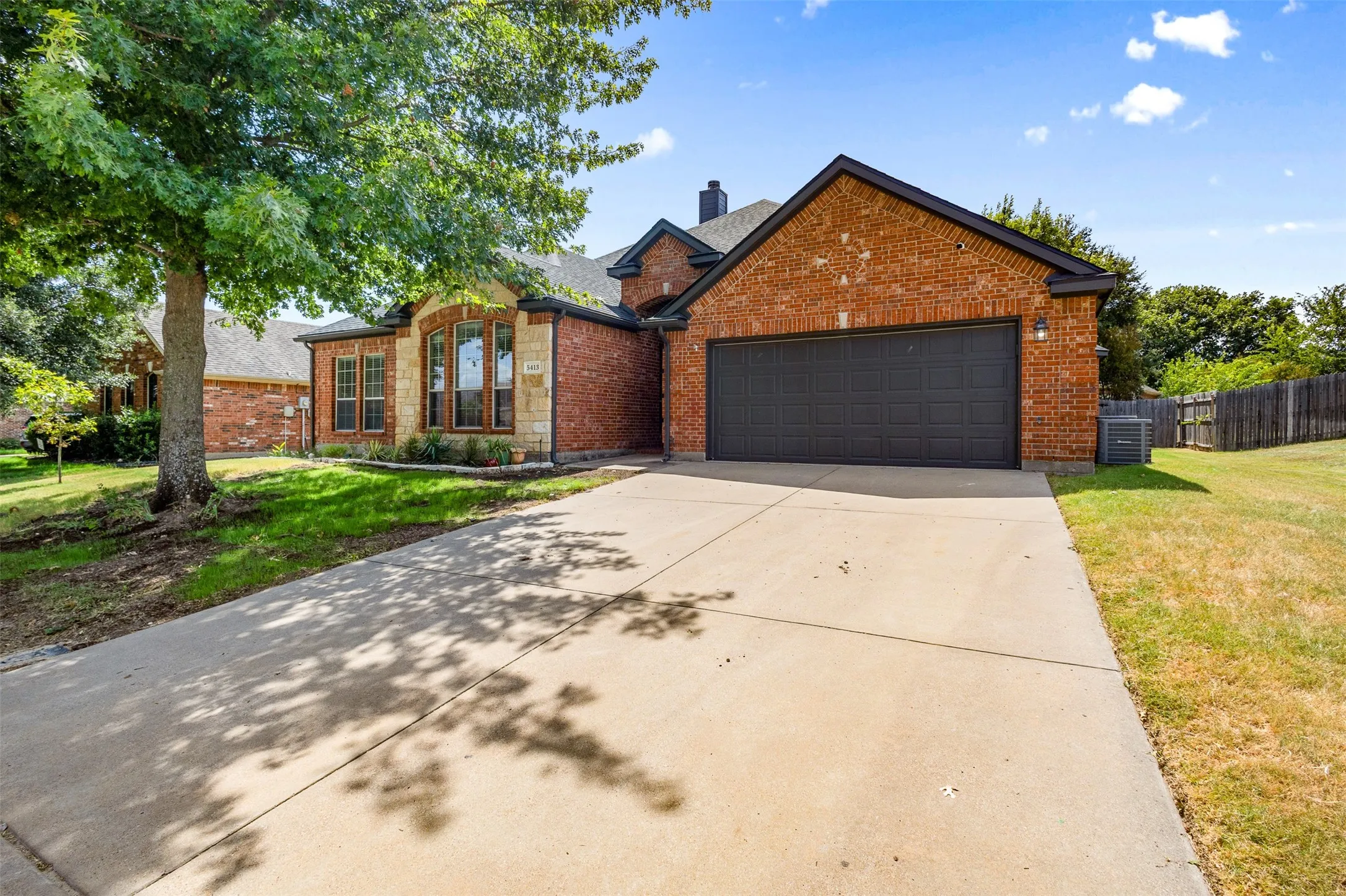 Brick exterior with stone accents, bay window, two-car garage, and mature landscaping