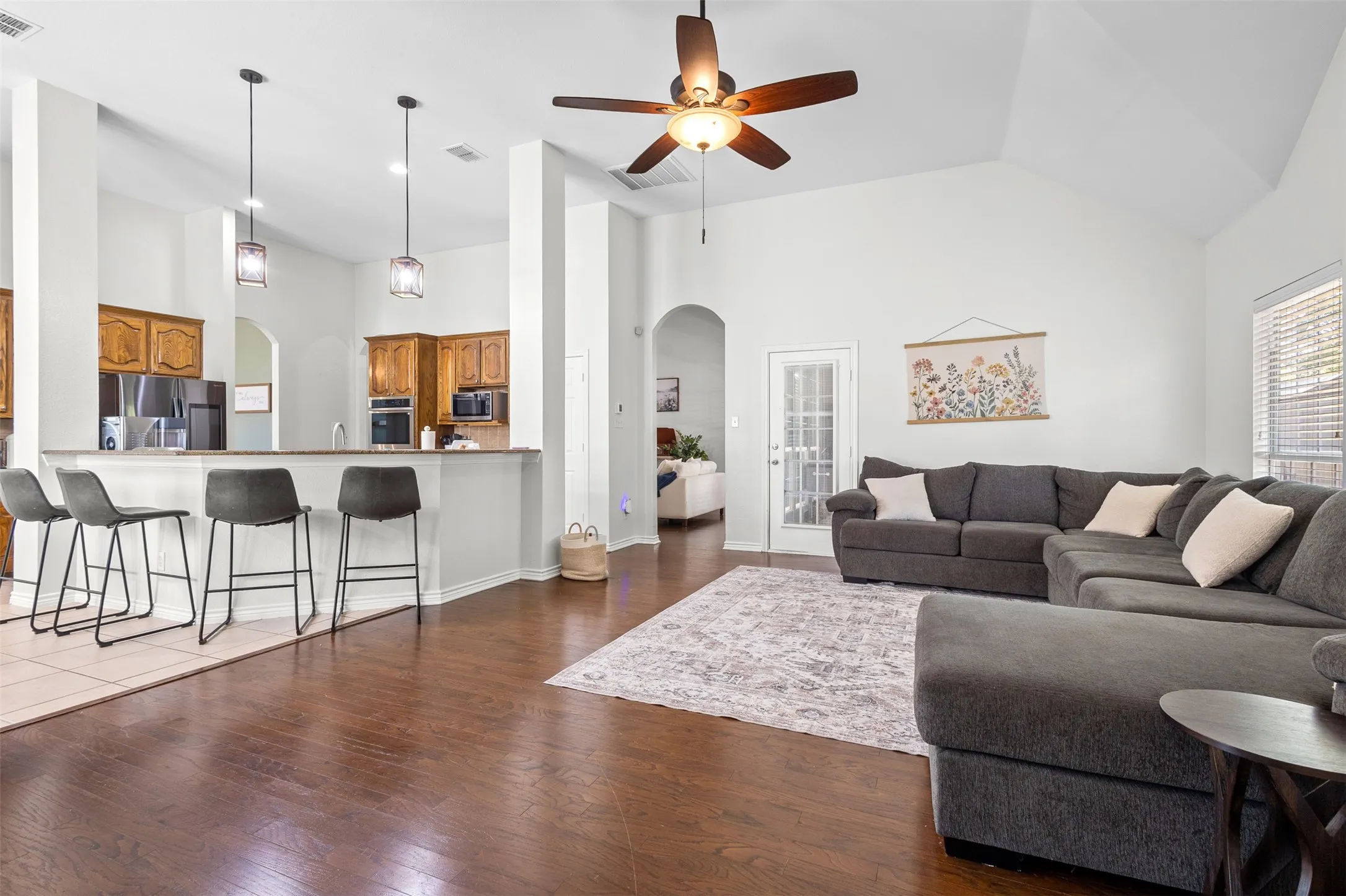 Vaulted ceilings, wood-finish flooring, recessed lighting, ceiling fan, and a kitchen pass-through with pendant lighting