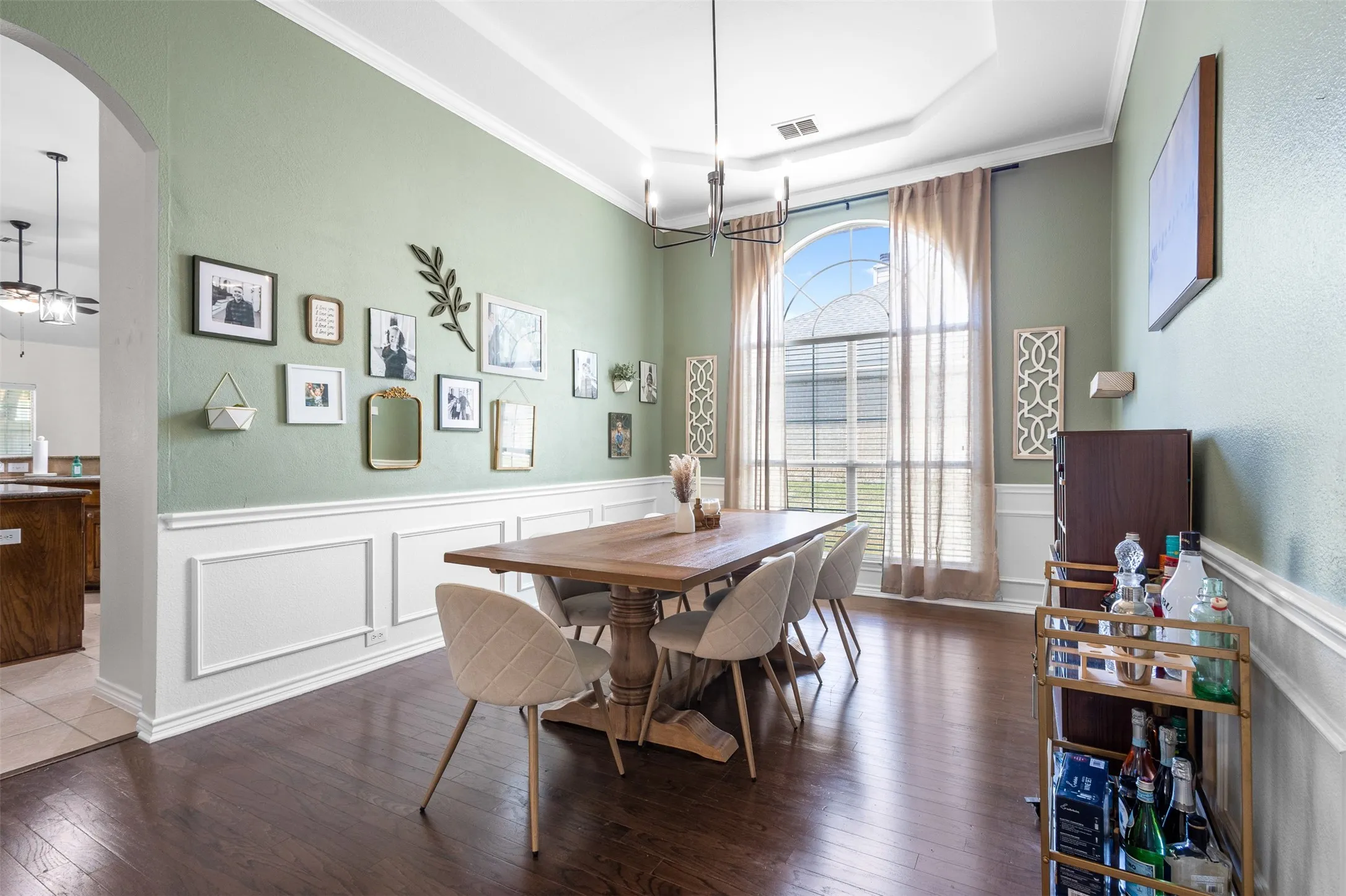 Tray ceiling with crown molding, wainscoting, wood-finish flooring, and an arched window