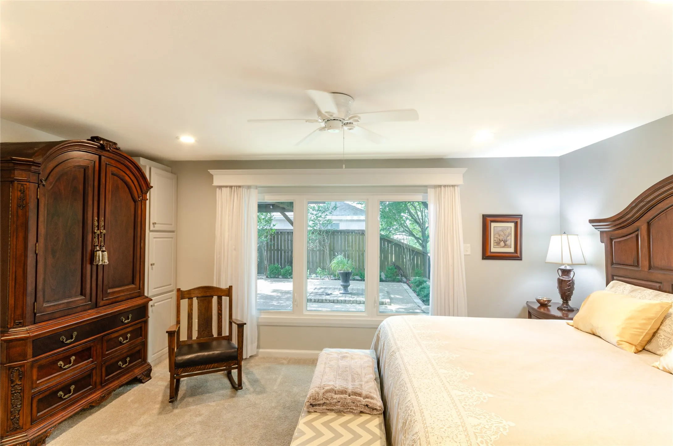 Recessed ceiling lighting, ceiling fan, carpeted flooring, built-in cabinetry, and a large window overlooking a paved patio