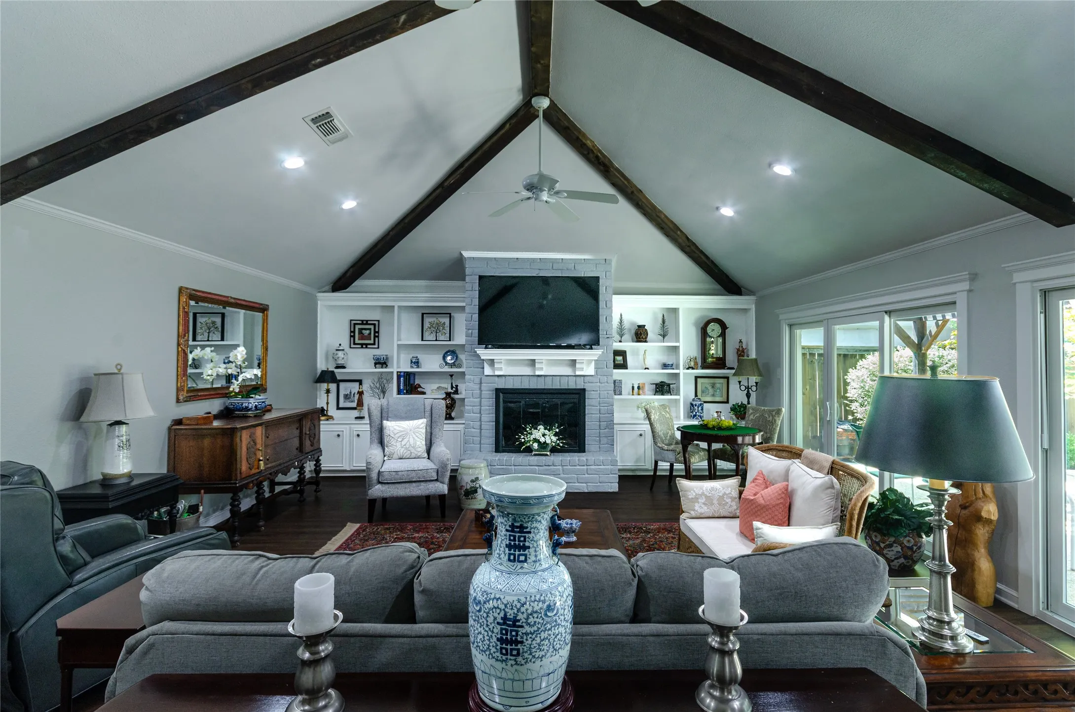 Vaulted ceiling with exposed wood beams, built-in shelving, brick fireplace with mantel, and sliding glass doors