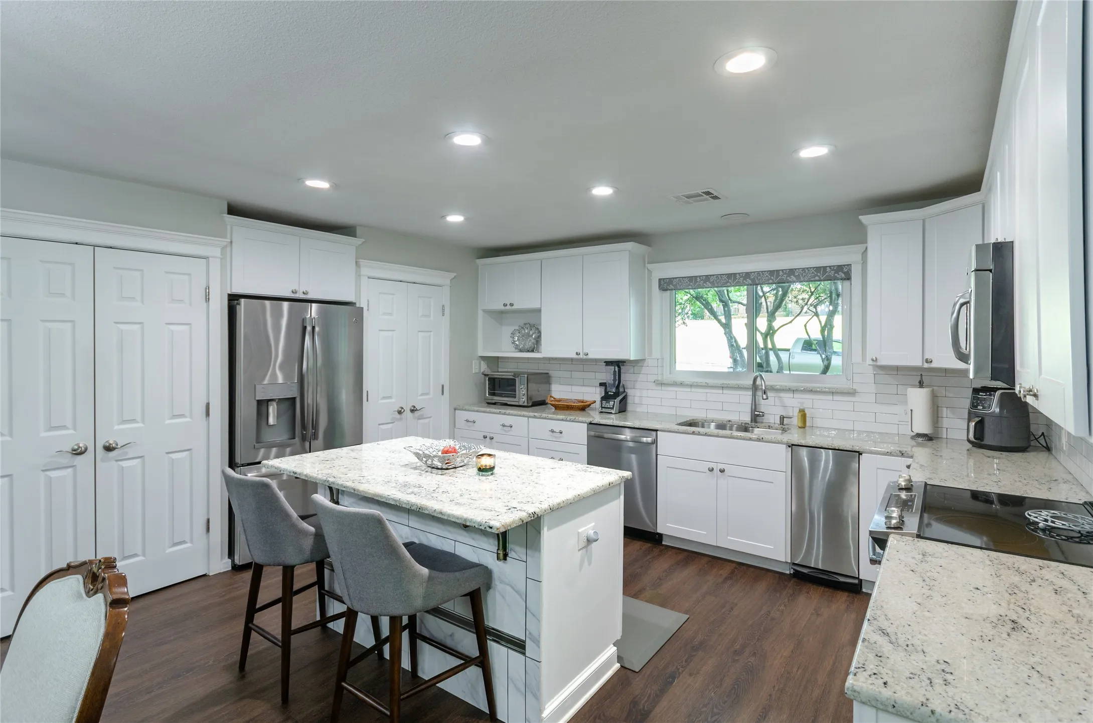 Kitchen featuring an island with a light-toned countertop, dark wood-finish flooring, white cabinetry, stainless steel appliances, and recessed lighting