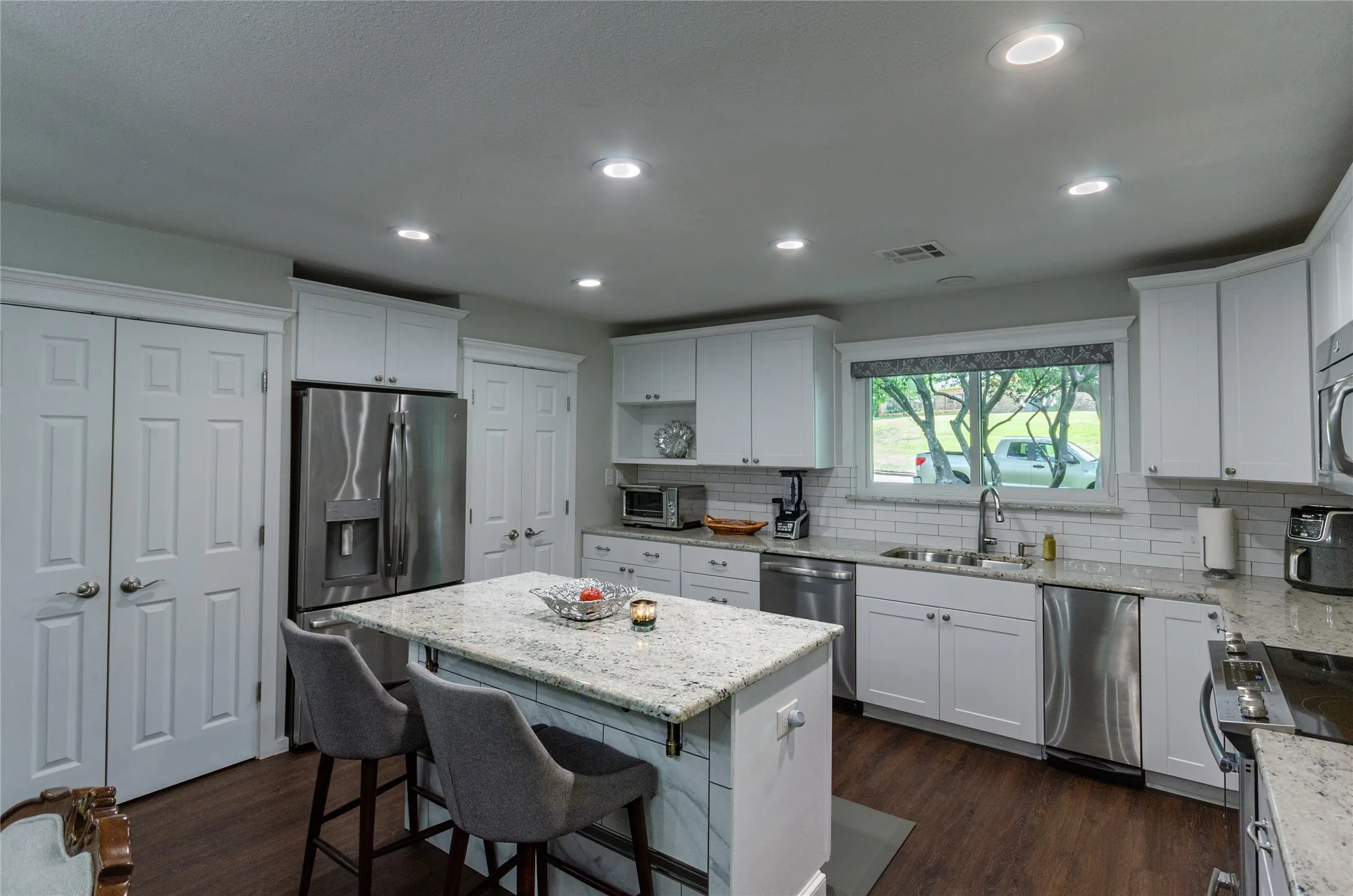 Kitchen featuring white cabinetry, granite countertops, stainless steel appliances, wood-finish flooring, and recessed lighting