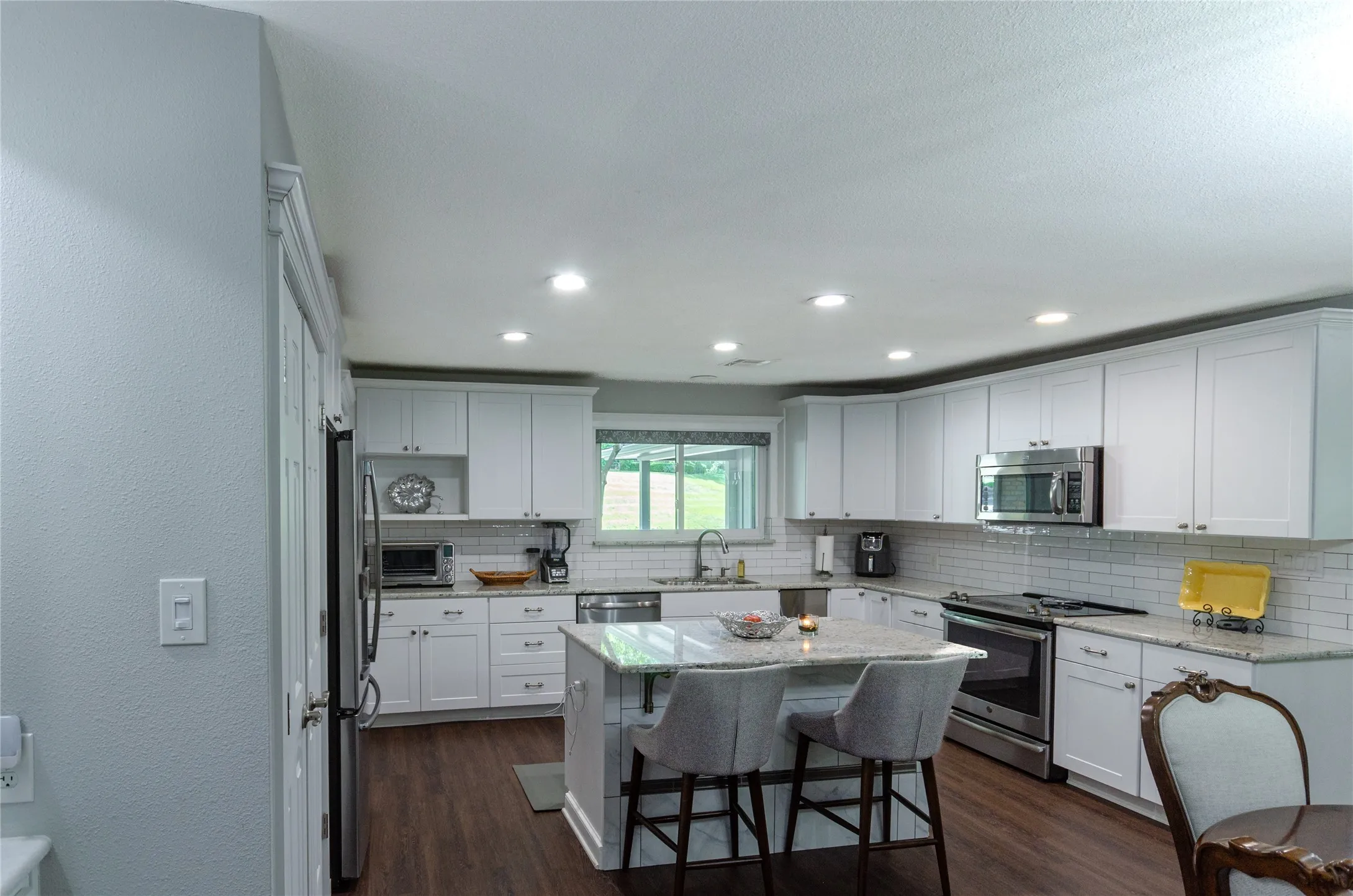 White shaker cabinetry, stainless steel appliances, wood-finish flooring, recessed lighting, and a kitchen island with seating