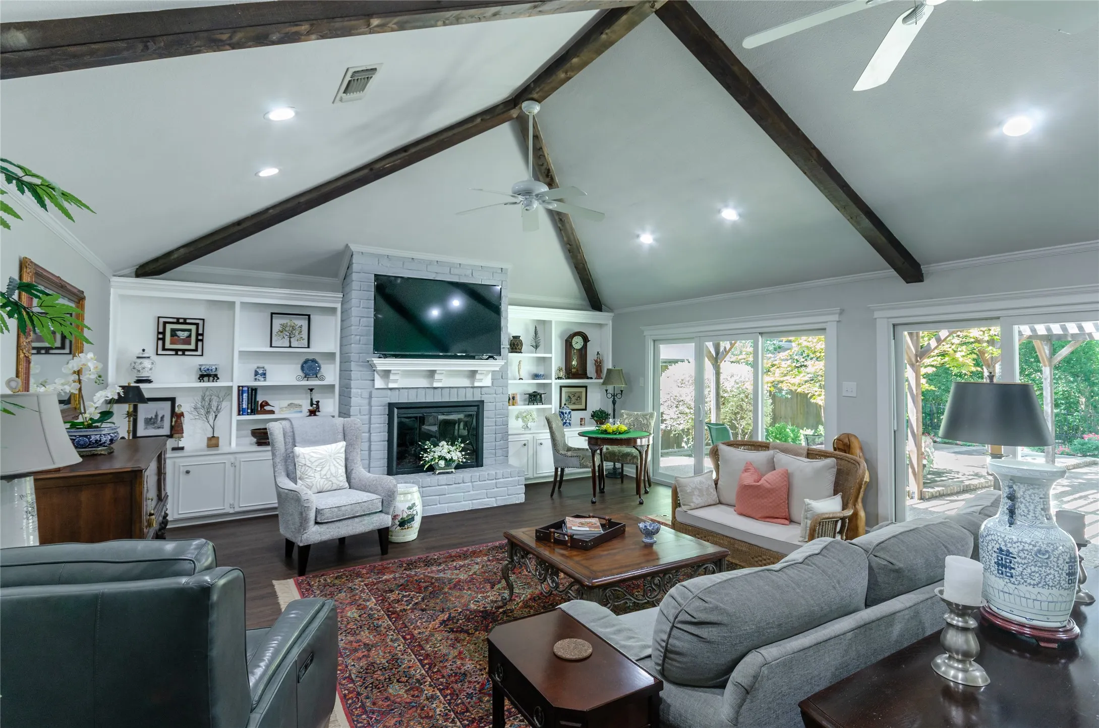 Vaulted ceiling with exposed wood beams, built-in shelving, brick fireplace, wood-finish flooring, and sliding glass doors