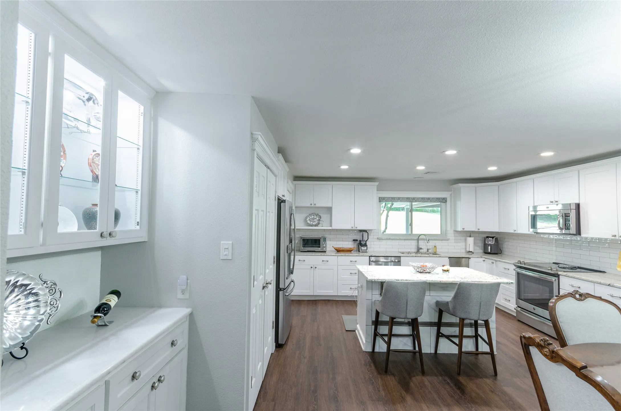 White cabinetry with glass-front uppers, stainless steel appliances, a center island with seating, and wood-finish flooring