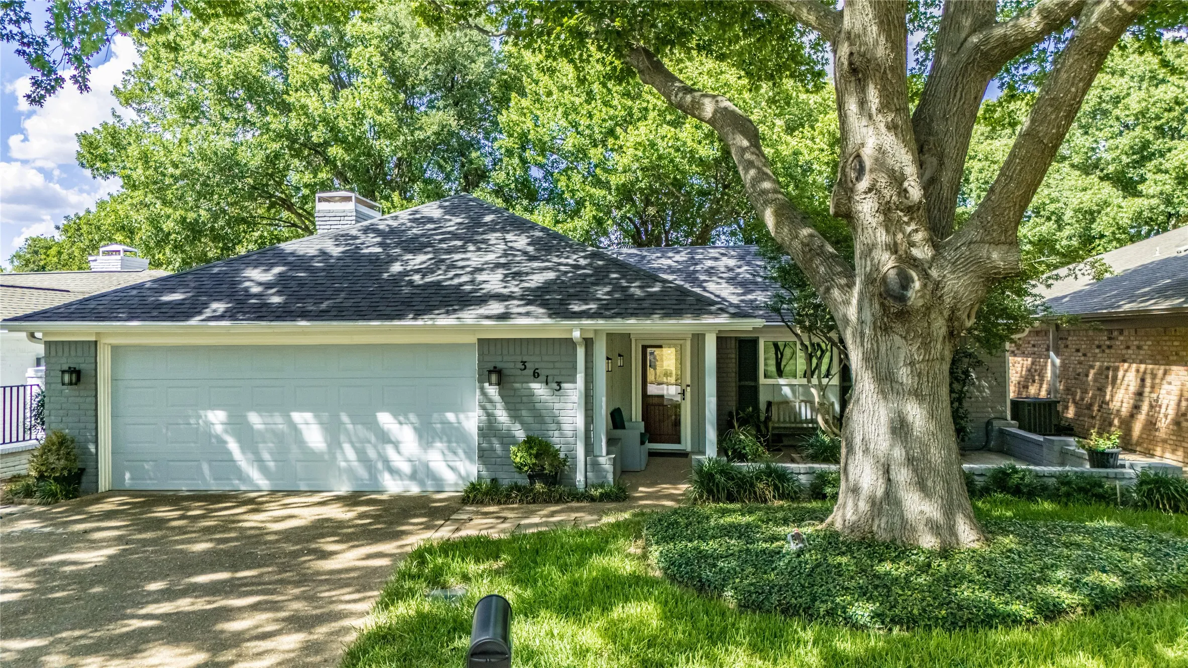 Brick exterior with an attached two-car garage, established front yard landscaping, and a mature tree