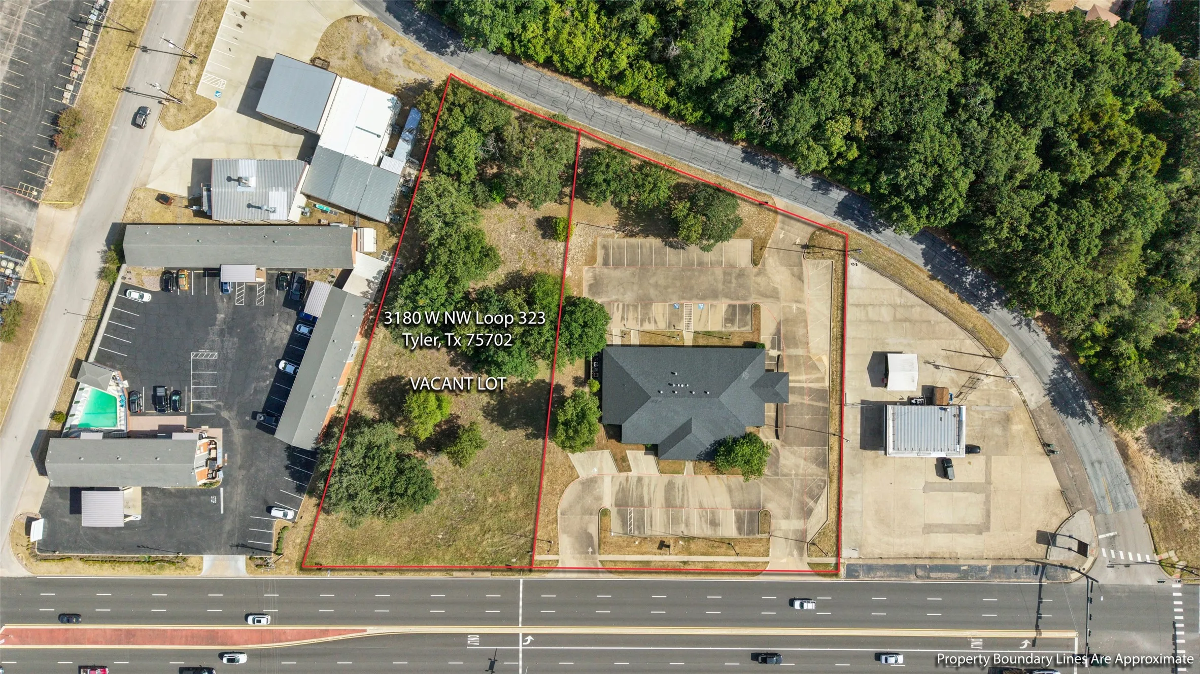 Property featuring a single-story building with a dark shingle roof, surrounded by extensive paved parking areas LISTED AT $799,000 Opportunity to expand! 3180 W NW LOOP 323 TYLER Adjacent 1.01-acre commercial lot available SEPARATELY for $110,000. Lot is NOT included in the building’s listed price.