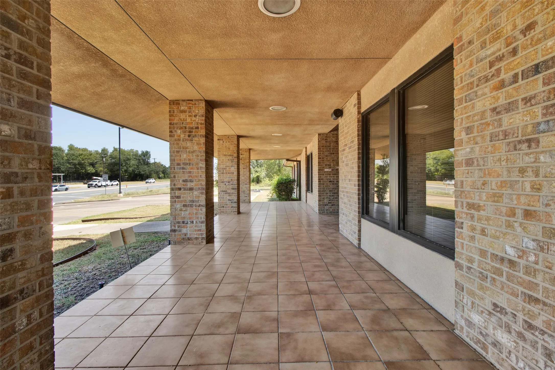 Brick exterior with a covered walkway, tiled flooring, recessed lighting, and large window openings