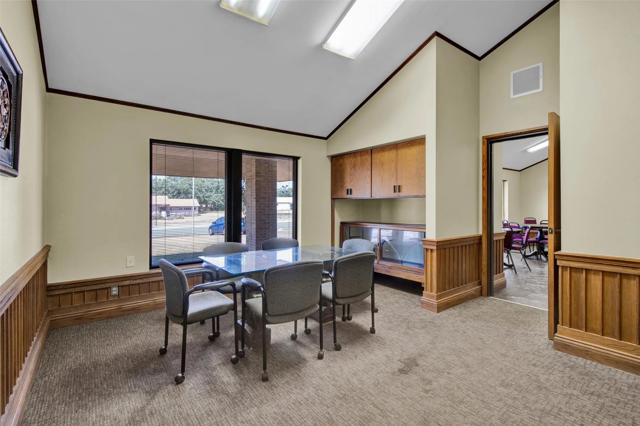 Vaulted ceiling, wood paneling, built-in cabinetry, large window, and carpeted flooring