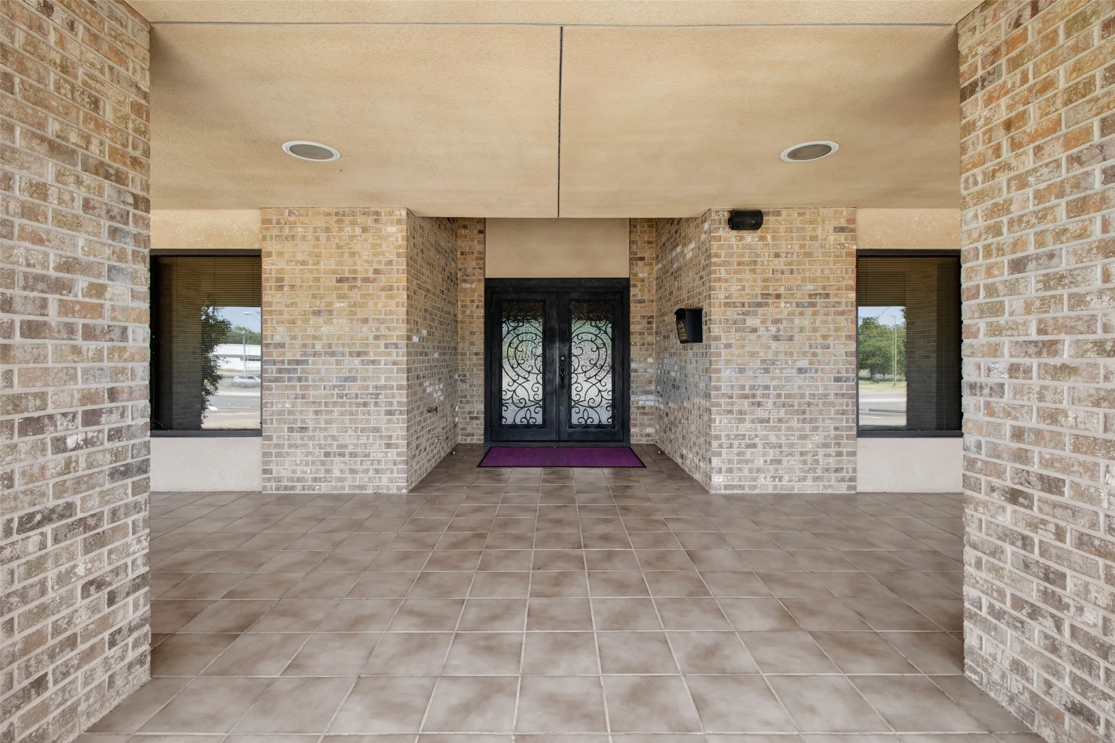 Brick exterior with a covered entry, tile flooring, and double entry doors with decorative glass inserts