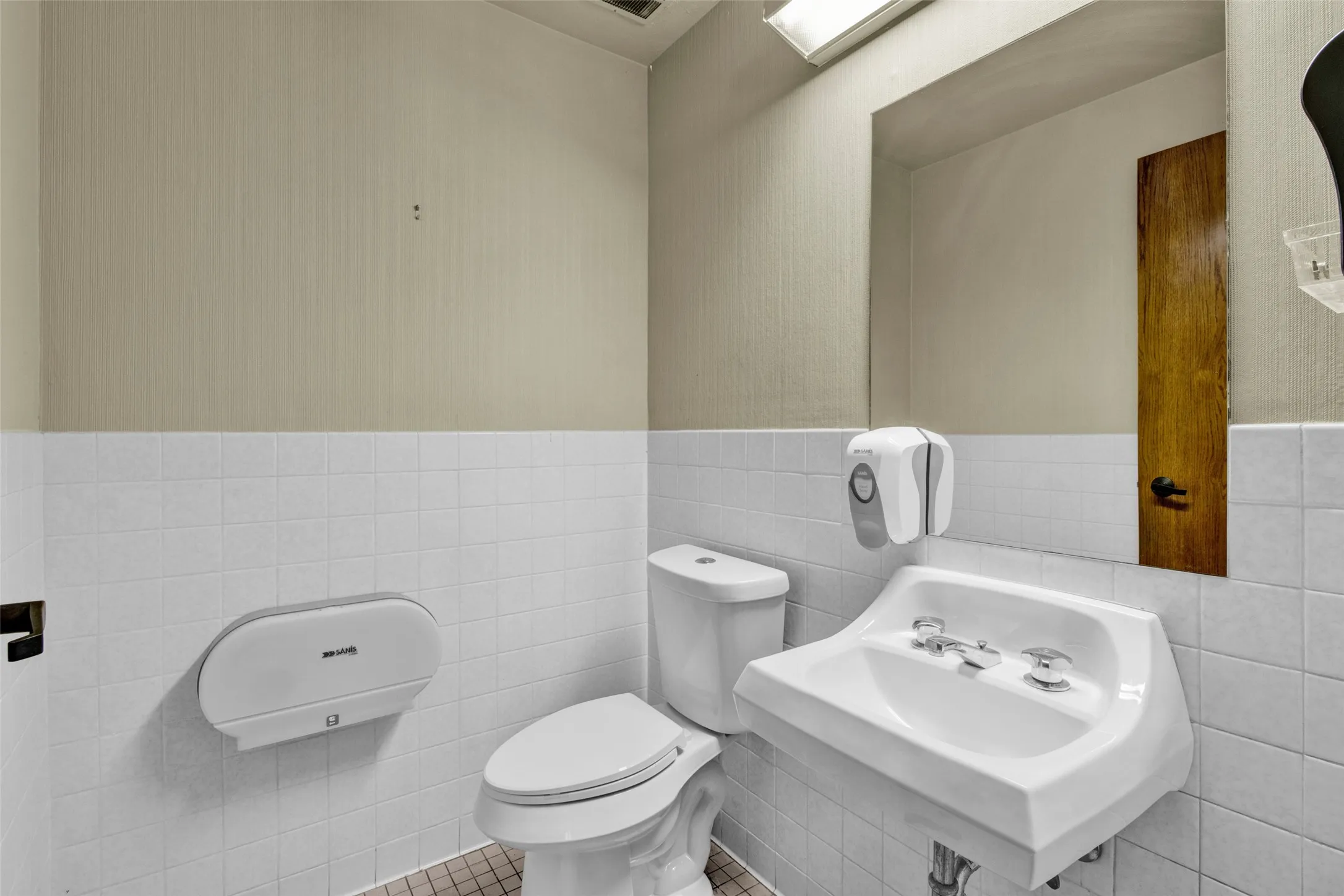 White tiled wall extending to mid-height, wall-mounted sink, and a commode