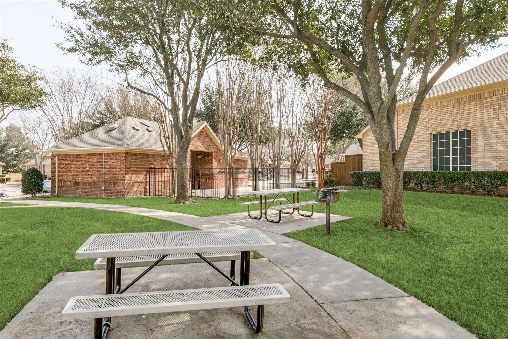 Manicured lawn area with concrete pathways, mature trees, and a brick-clad structure