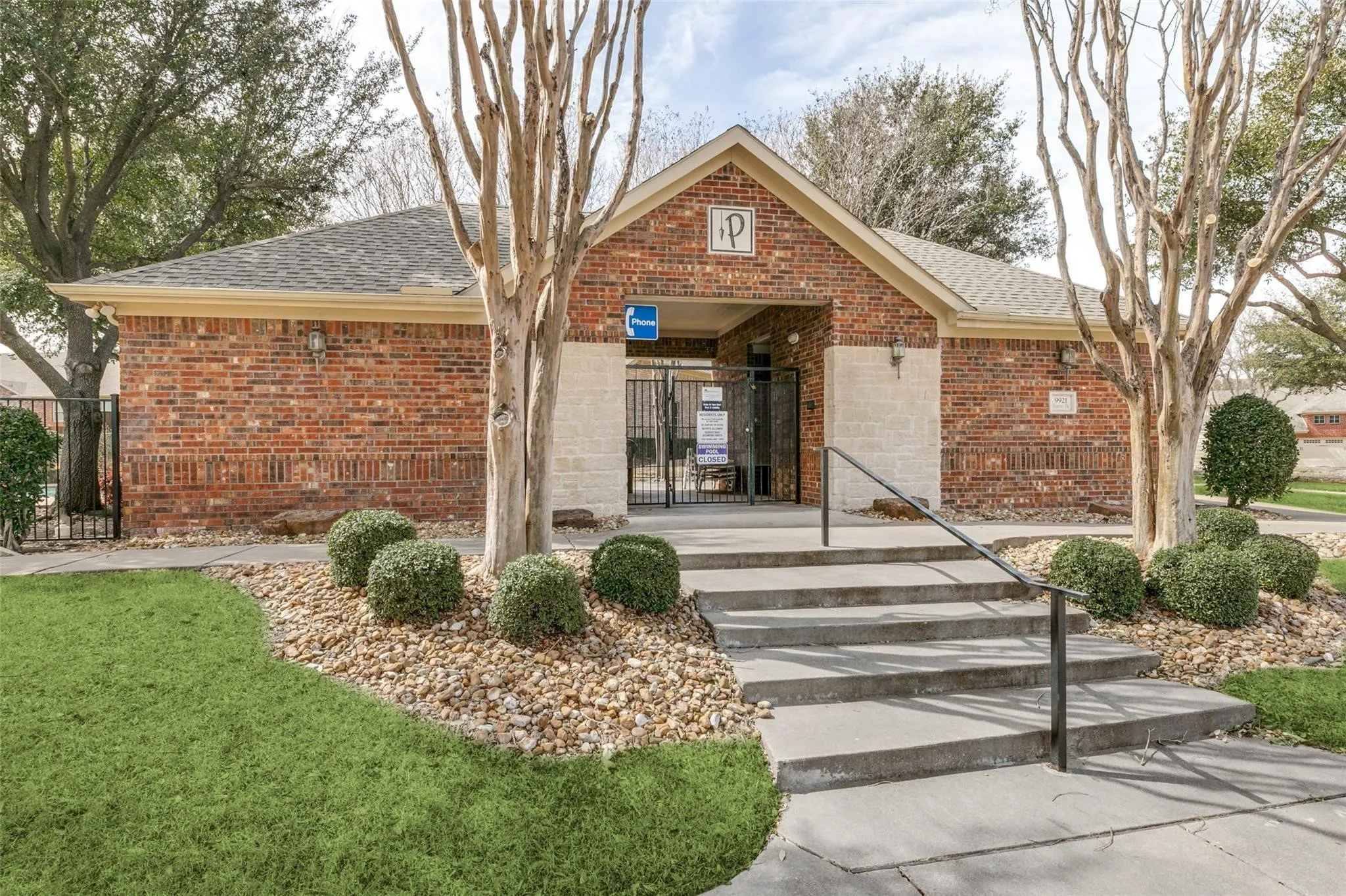 Brick exterior building with gabled entry, concrete steps, black metal handrails, and a black metal gate