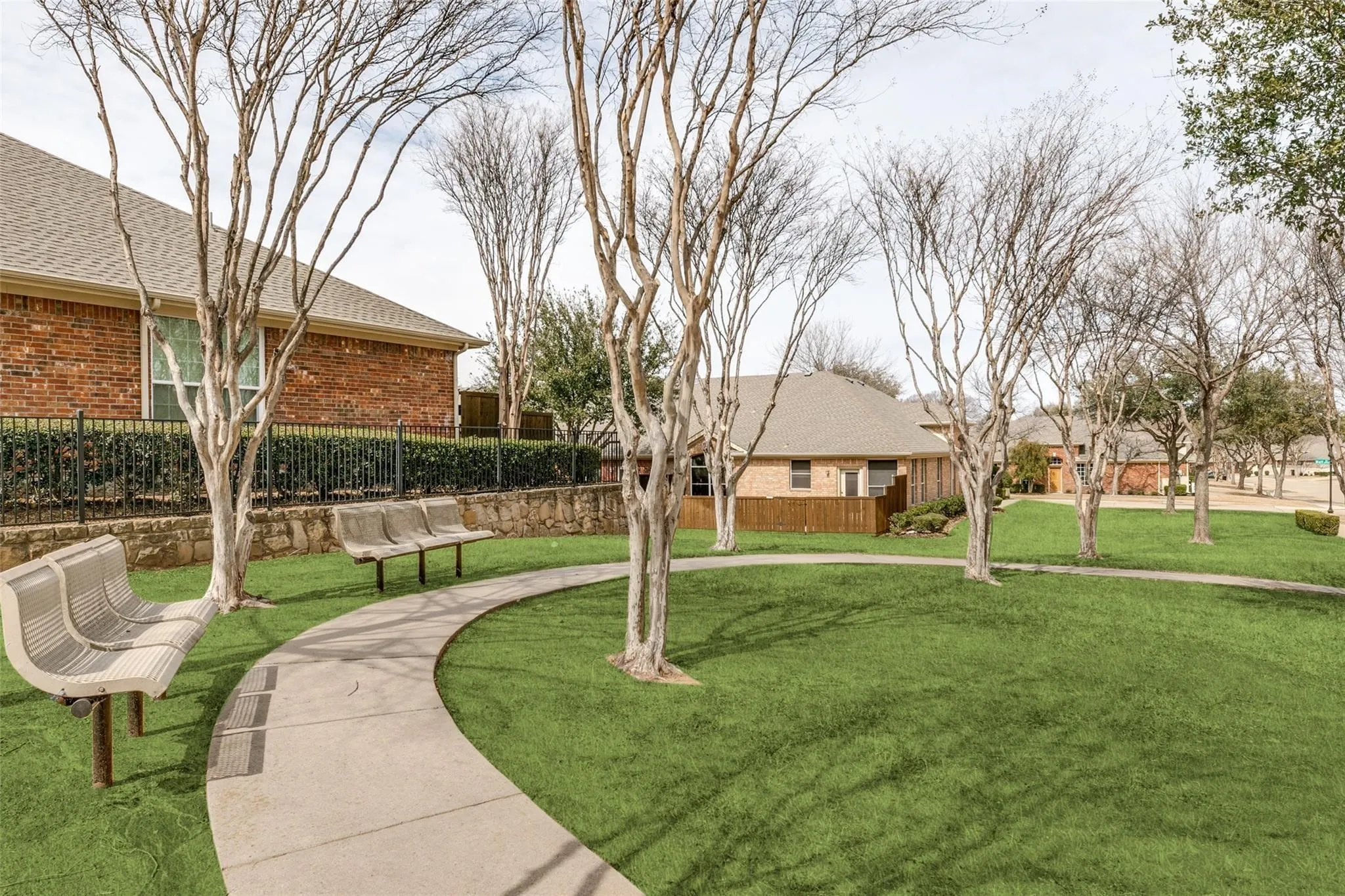 Manicured green space with mature trees, curved concrete pathway, and multiple benches
