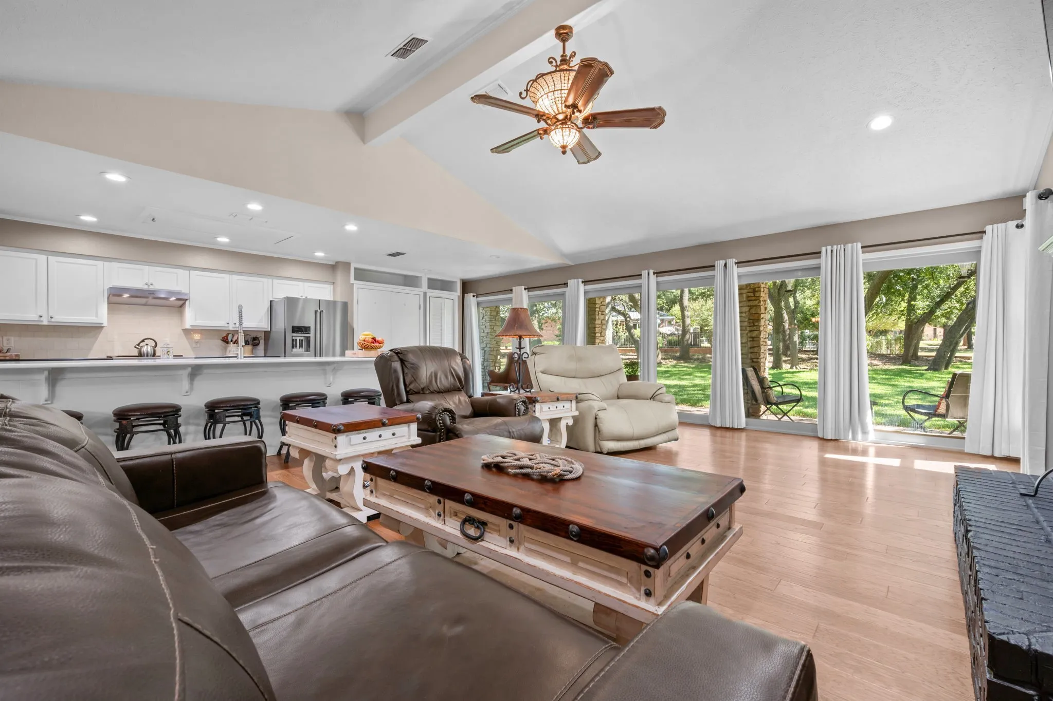 Vaulted ceiling with an ornate ceiling fan, wood-finish flooring, a wall of glass doors, a kitchen breakfast bar, and white kitchen cabinetry