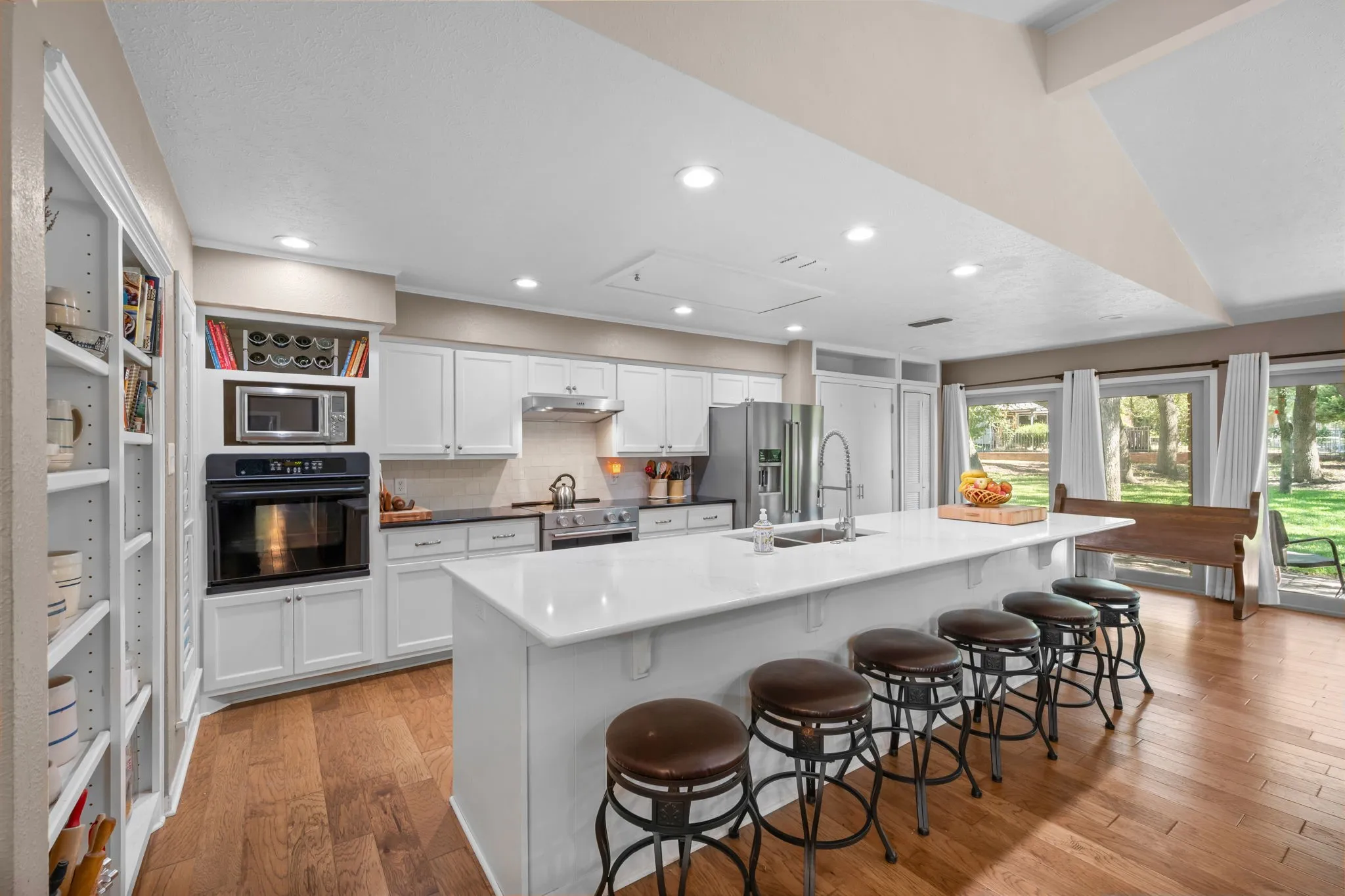 Spacious kitchen featuring white cabinetry, a large center island with seating, stainless steel appliances, built-in shelving, and wood-finish flooring