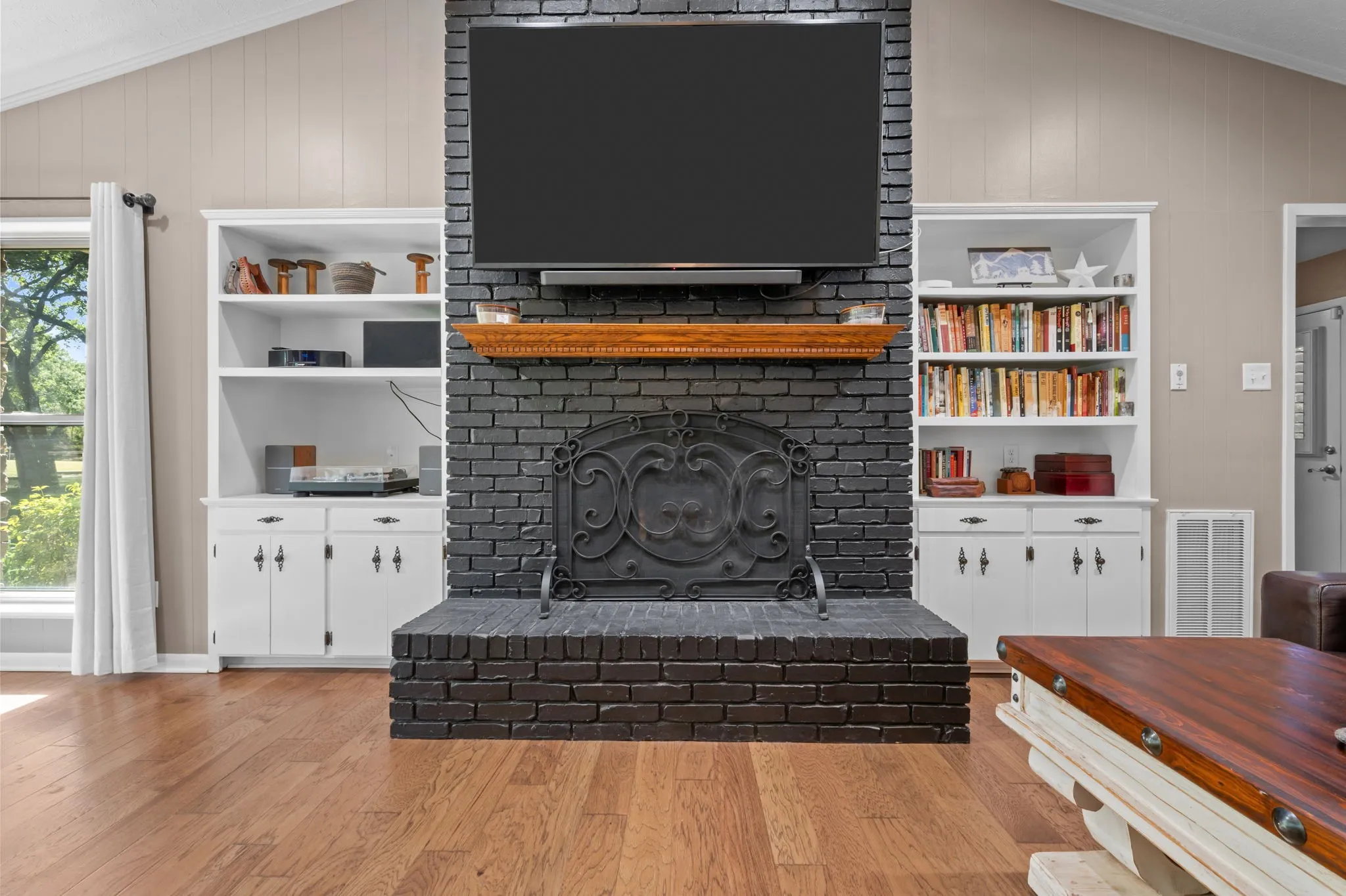 Central brick fireplace with a wood-finish mantel, flanked by built-in shelving and cabinetry, and wood-finish flooring