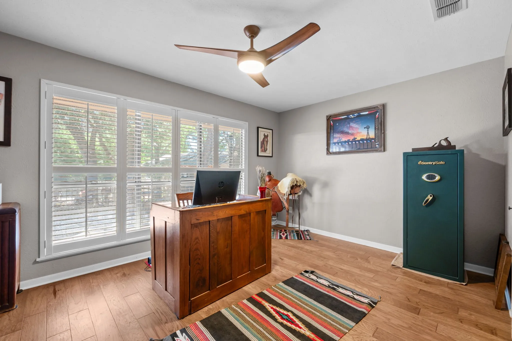 Wood-finish flooring, multiple windows with white blinds, and a ceiling fan with integrated lighting