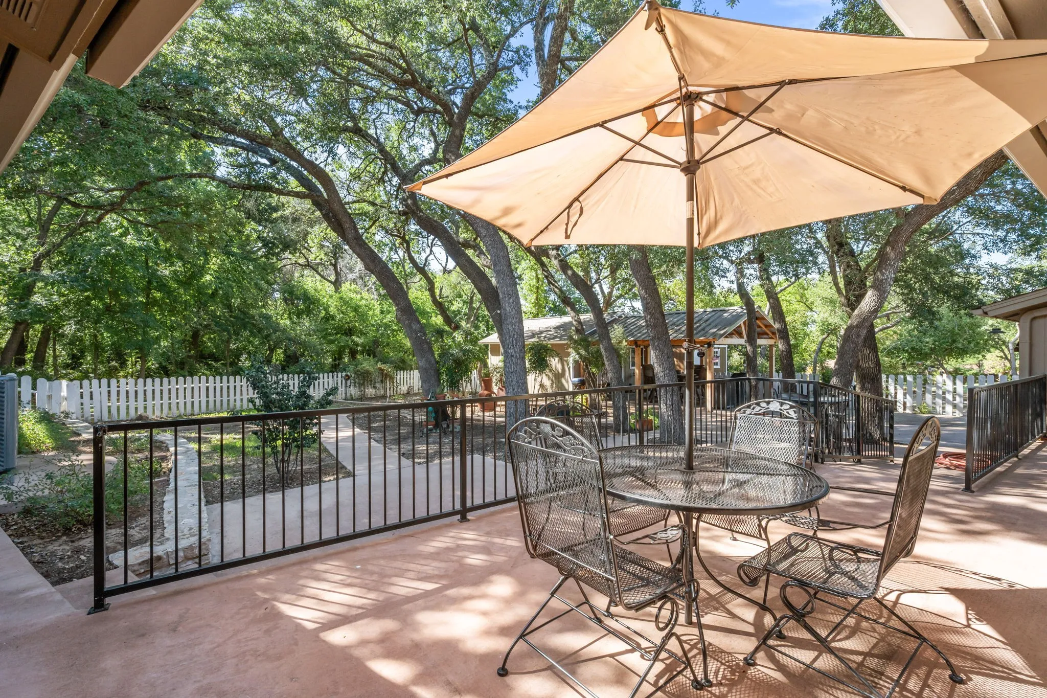 Patio featuring a concrete surface, black metal railing, and a mature tree canopy