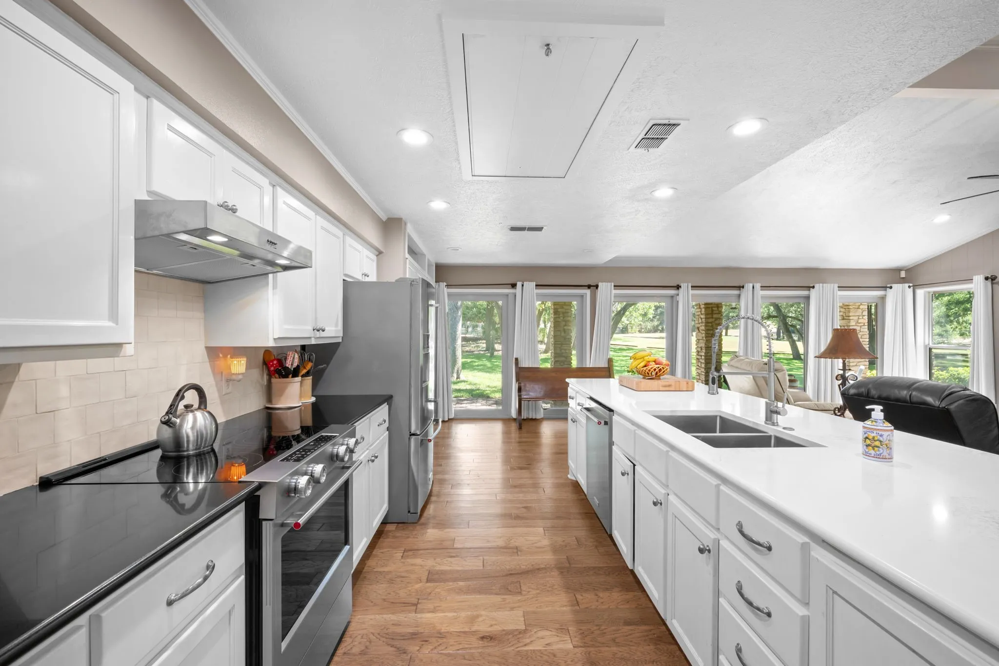 White cabinetry with stainless steel hardware, black countertop, stainless steel appliances, large kitchen island with double sink, and wood-finish flooring
