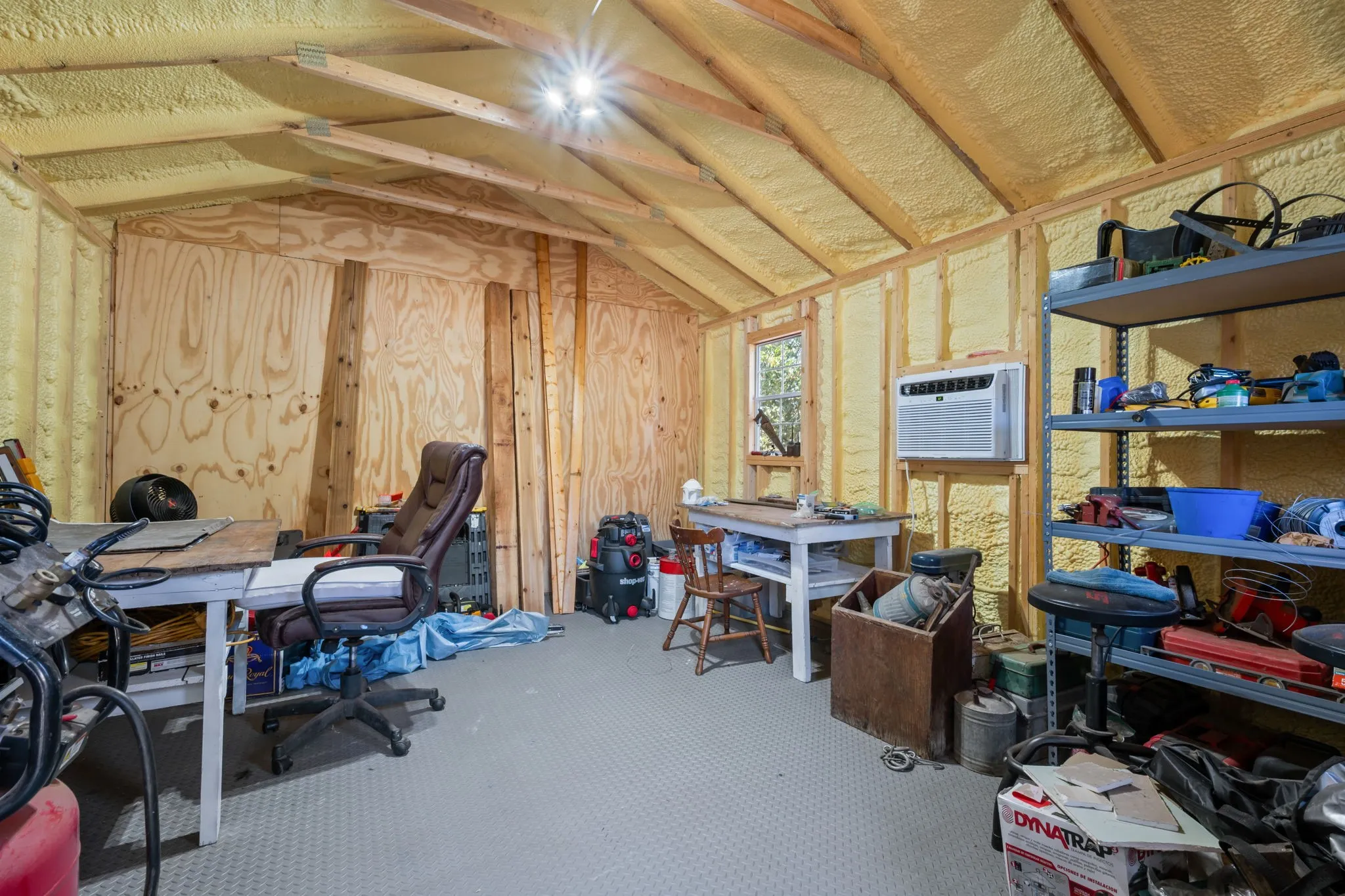 Utility structure featuring exposed wood paneling, spray foam insulation, and a mounted air conditioning unit