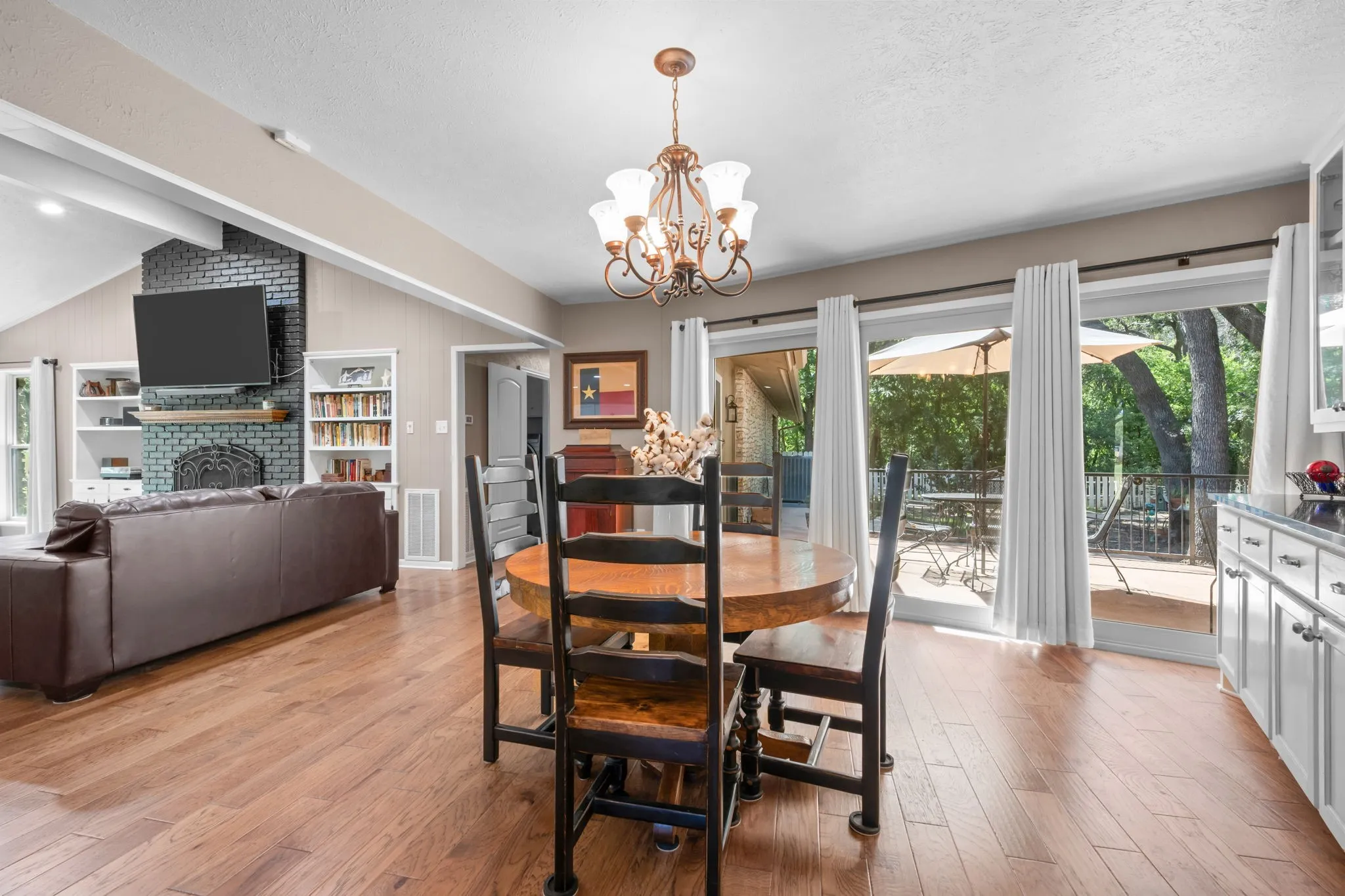 Hardwood-style flooring throughout, vaulted ceiling, built-in shelving, brick fireplace, and sliding glass doors to outdoor deck