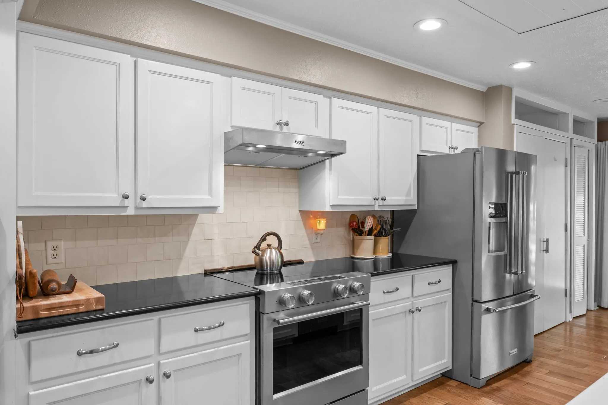 White cabinetry with brushed nickel hardware, black countertops, stainless steel appliances, and a tiled backsplash