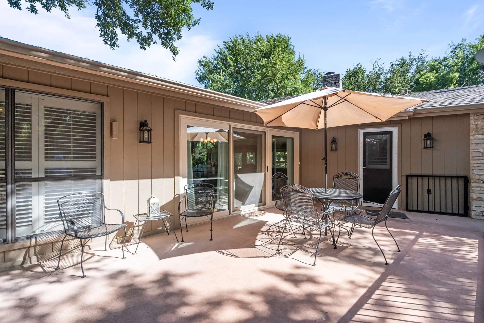 Expansive concrete patio with direct access via sliding glass doors, featuring exterior sconce lighting and a stone-clad wall accent