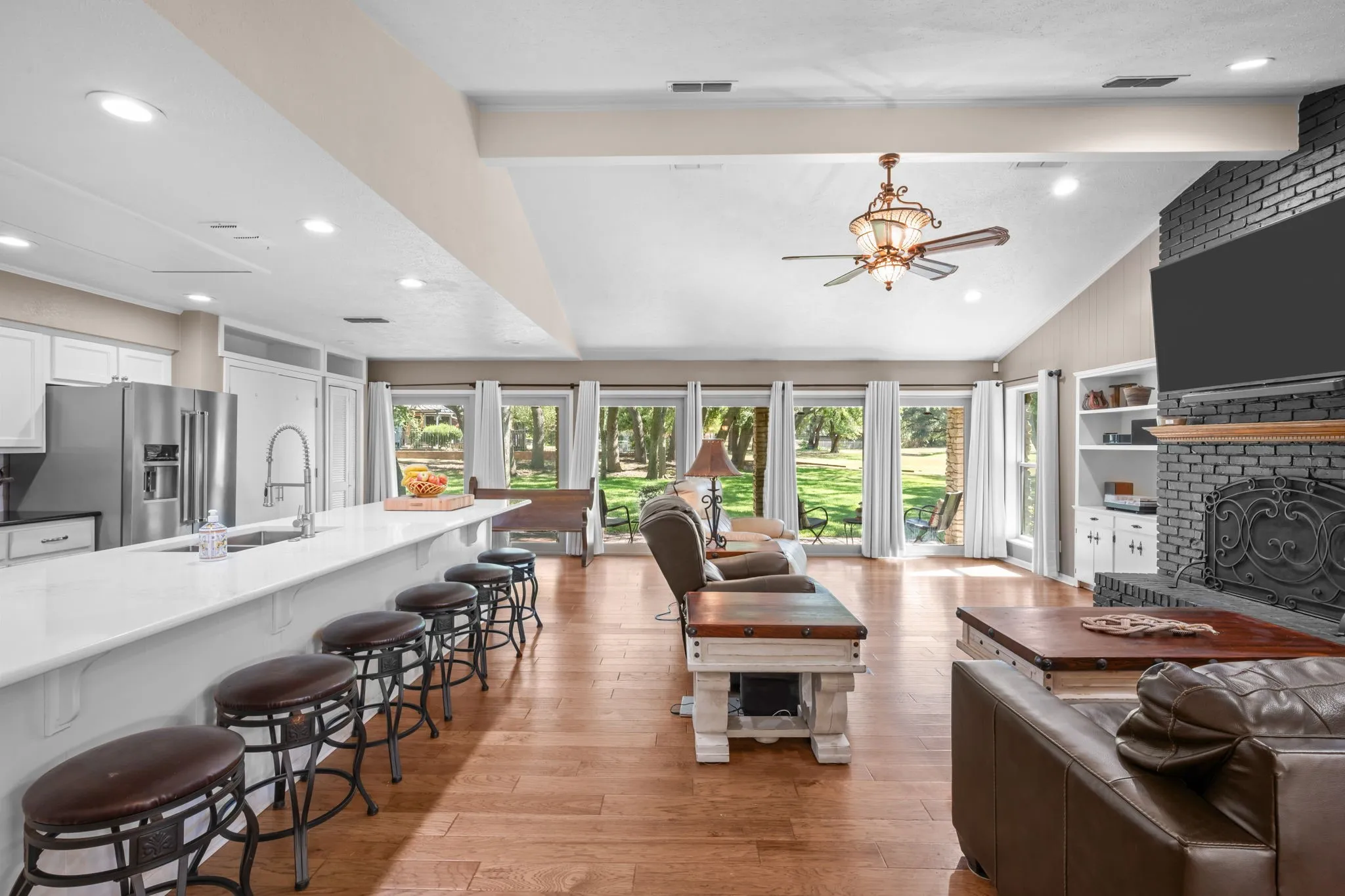 Vaulted ceiling with an ornate ceiling fan, recessed lighting, wood-finish flooring, white cabinetry, and a black brick fireplace with built-in shelving