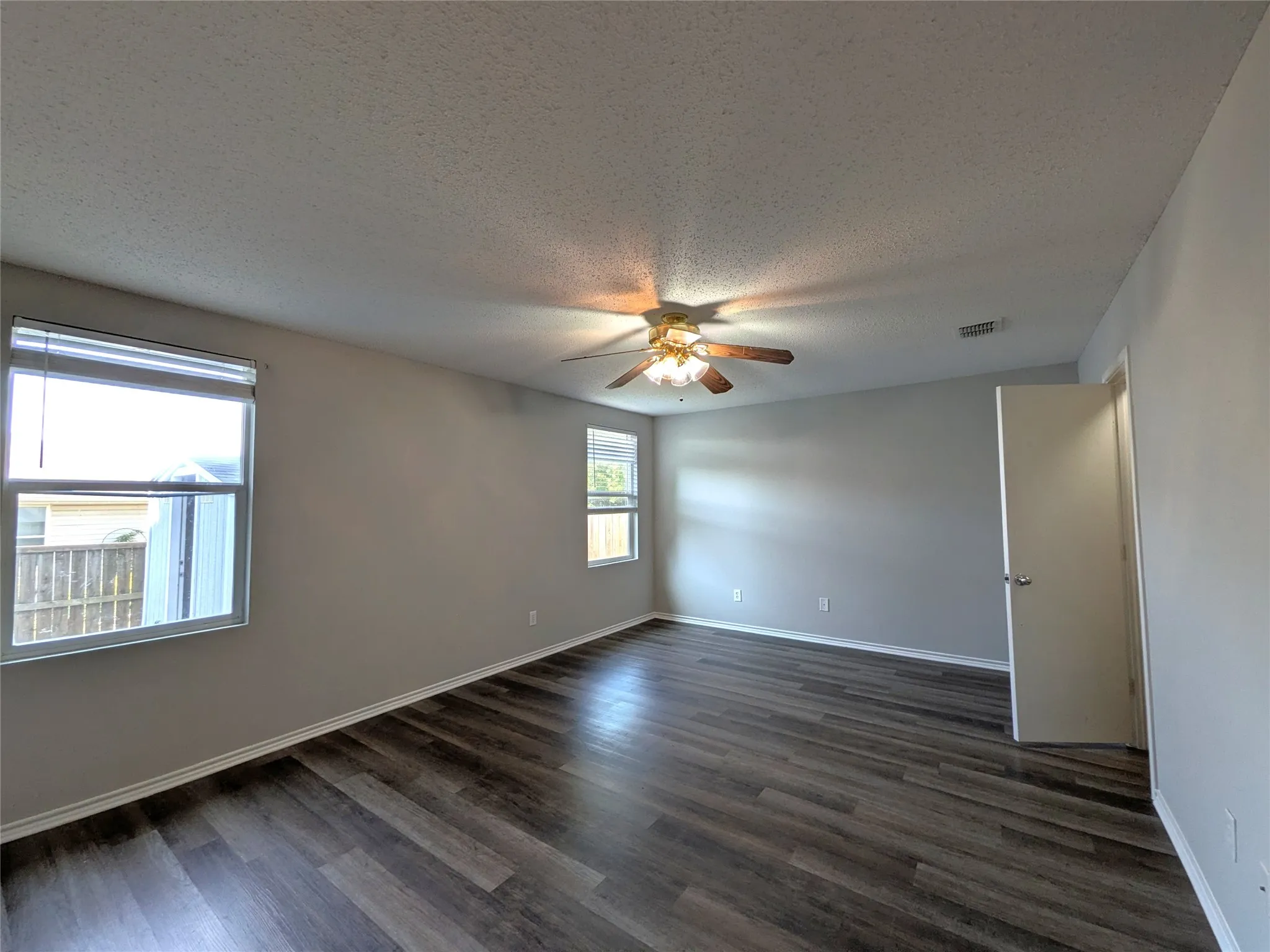 Wood-finish flooring, neutral wall tones, two windows with blinds, a ceiling fan with integrated lighting, and a white interior door