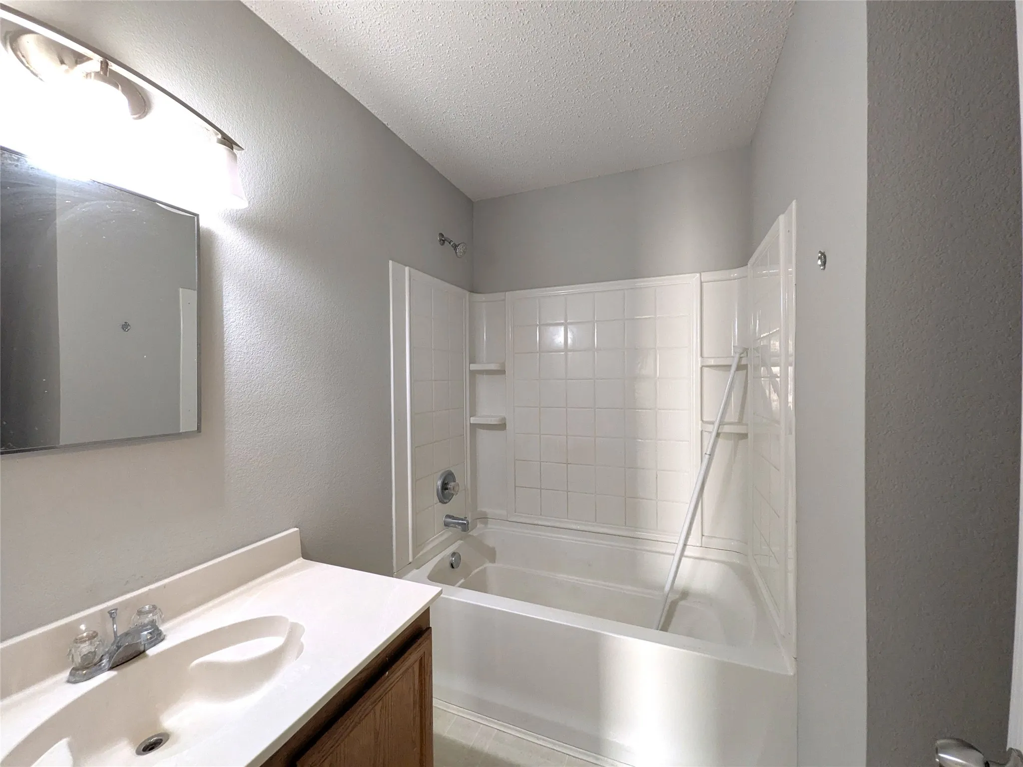 Bathroom featuring a white bathtub, ceramic tile surround, vanity with an integrated sink, wall-mounted mirror, and overhead lighting
