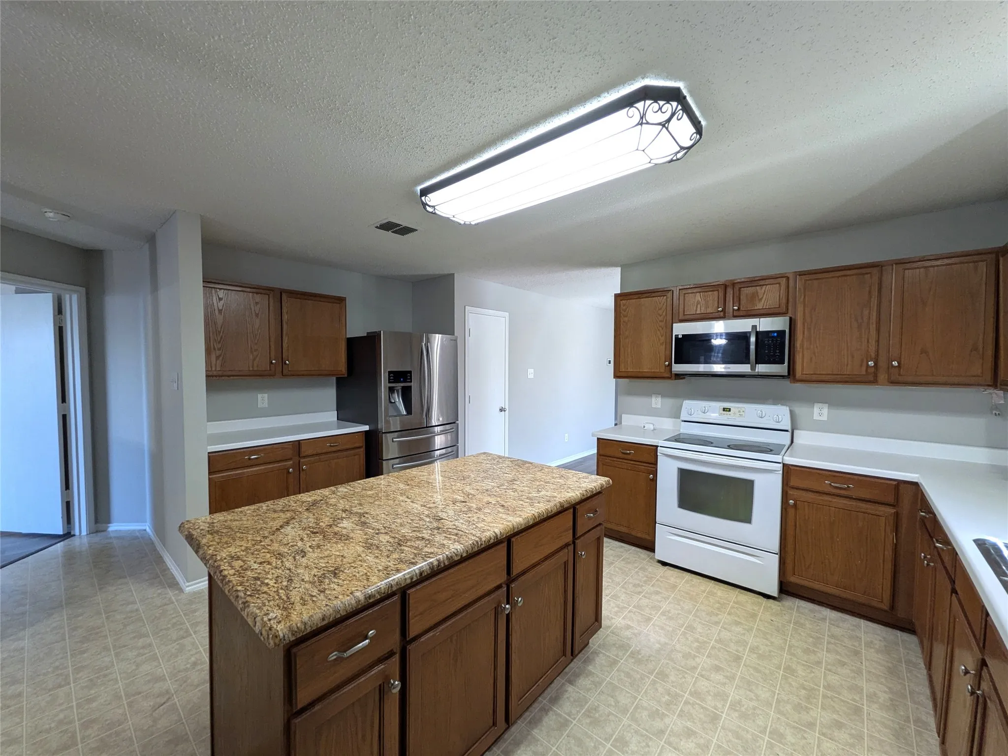 Kitchen featuring wood-finish cabinetry, a central island with a stone-finish countertop, stainless steel refrigerator, and white appliances