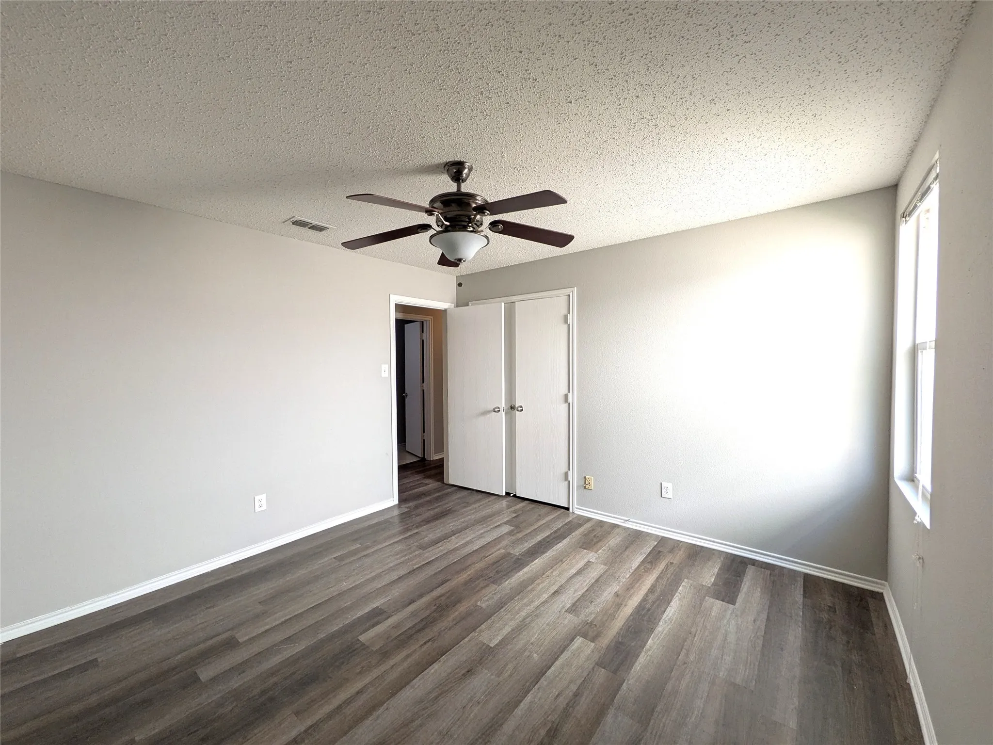 Wood-finish flooring, light gray wall paint, white trim, ceiling fan with integrated lighting, and a double-door closet