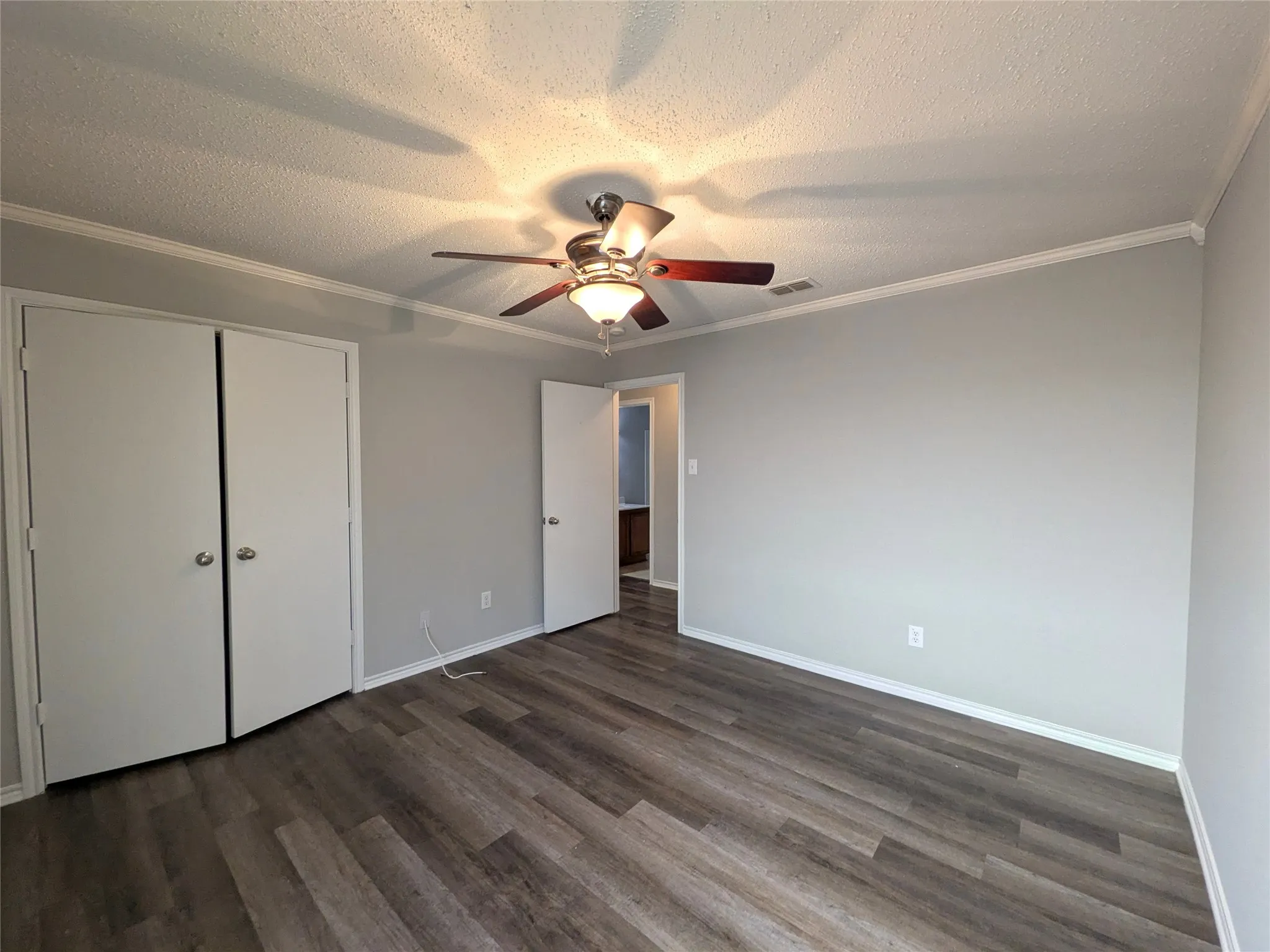 Wood-finish flooring, light grey painted walls, white crown molding, ceiling fan with integrated lighting, and a bi-fold closet