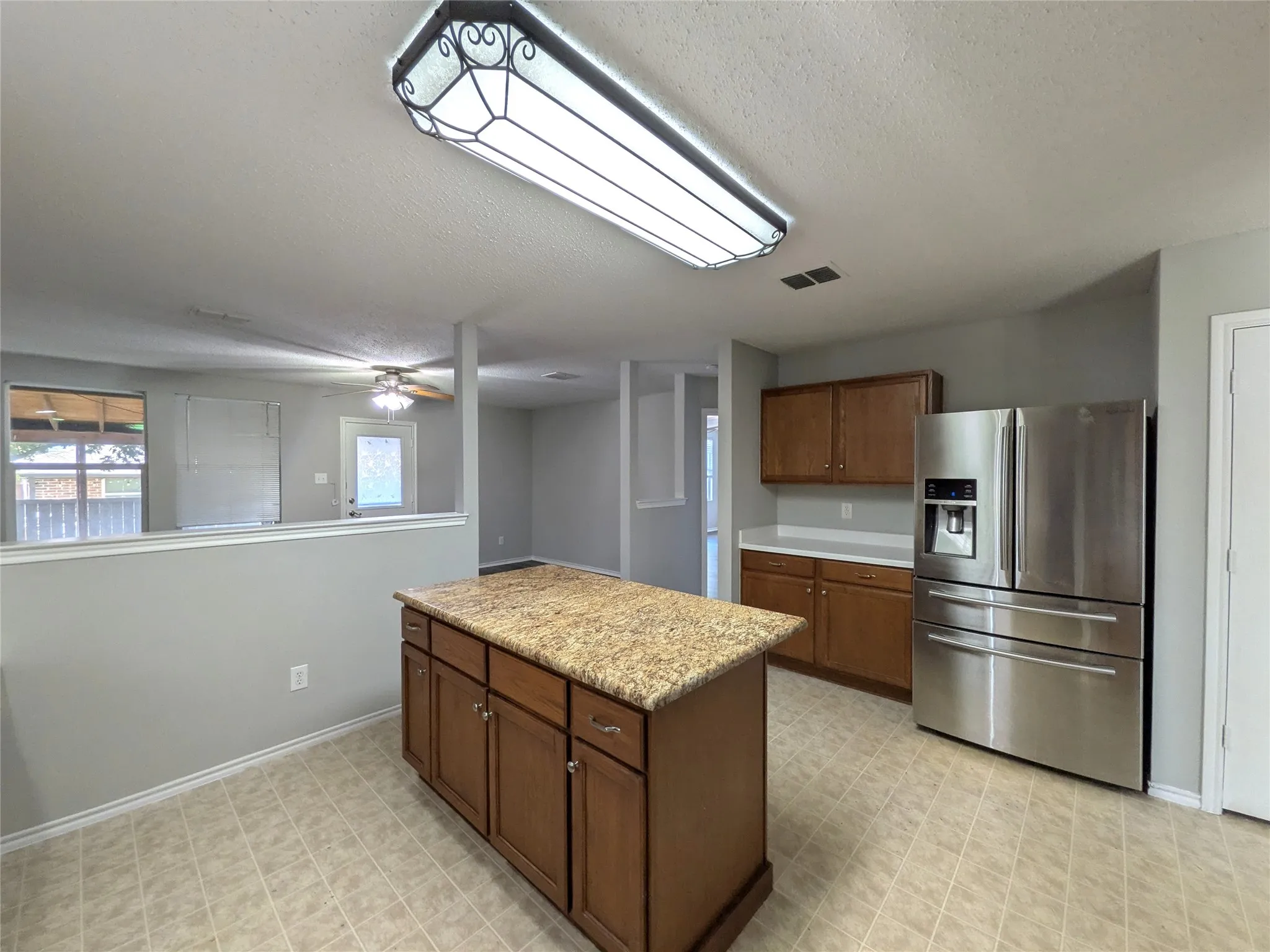 Kitchen featuring a central island with a stone-finish countertop, wood cabinetry, and stainless steel refrigerator