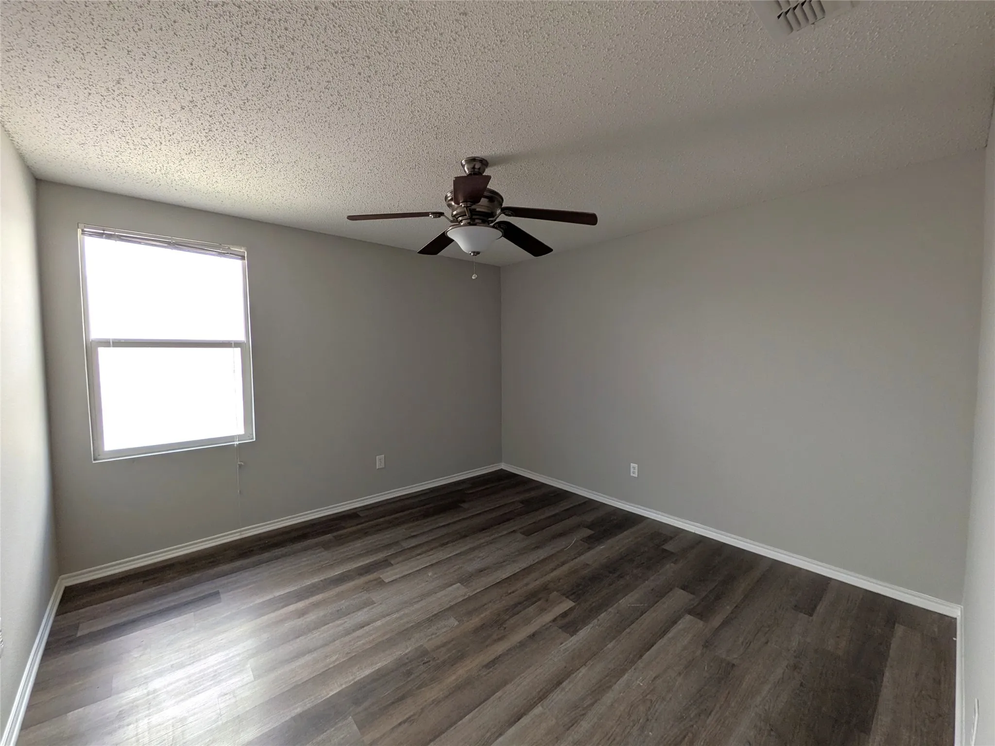 Room featuring wood-finish flooring, a ceiling fan with integrated lighting, and a window with blinds