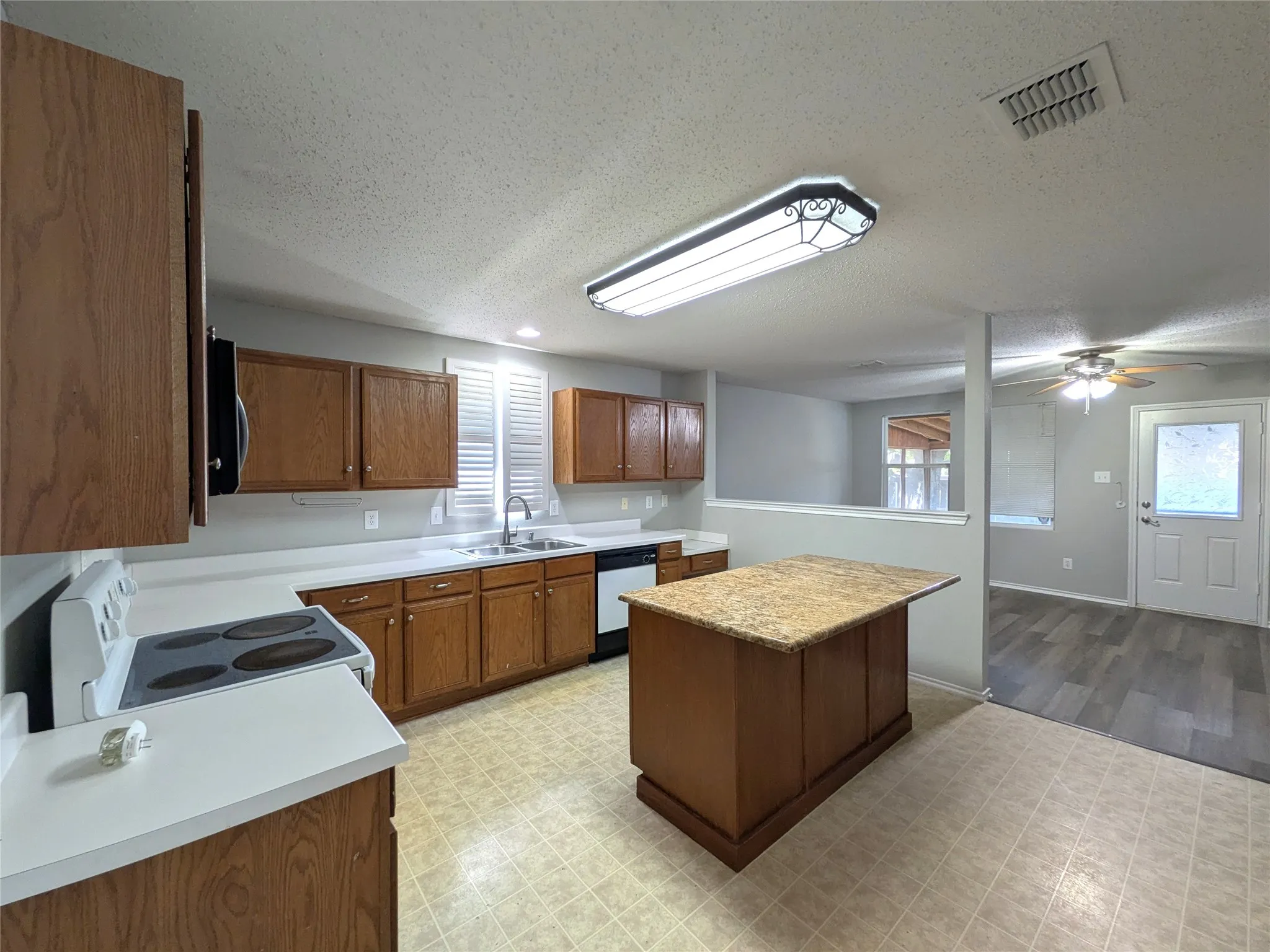 Kitchen featuring wood cabinetry, white countertops, a central island with a stone-finish top, and a stainless steel sink